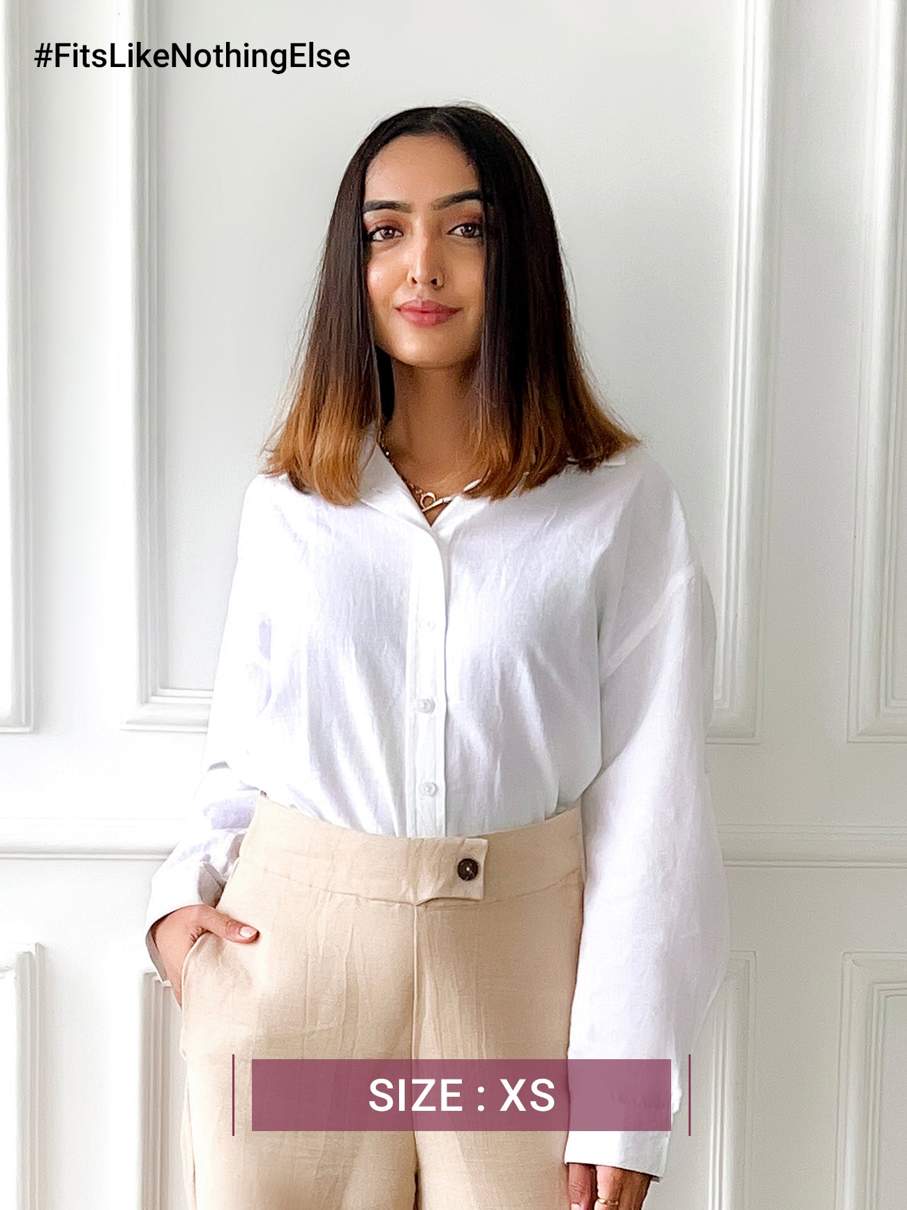 A woman smiling, wearing a white oversized collared shirt with long sleeves and a button placket.