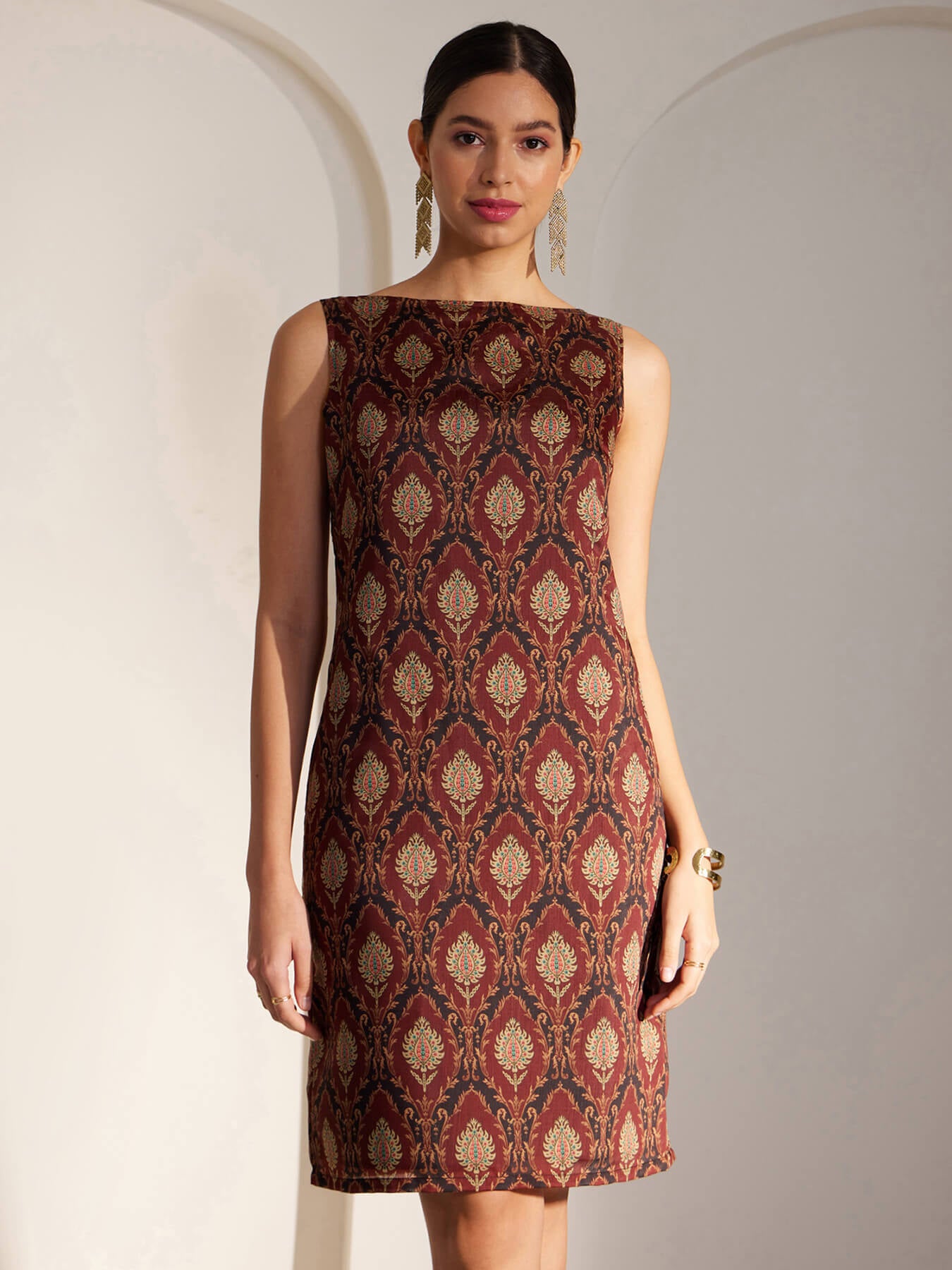 A woman wearing a sleeveless maroon shift dress with an Indian motif print.