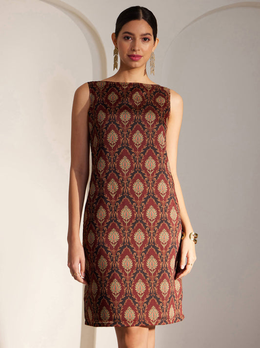 A woman wearing a sleeveless maroon shift dress with an Indian motif print.