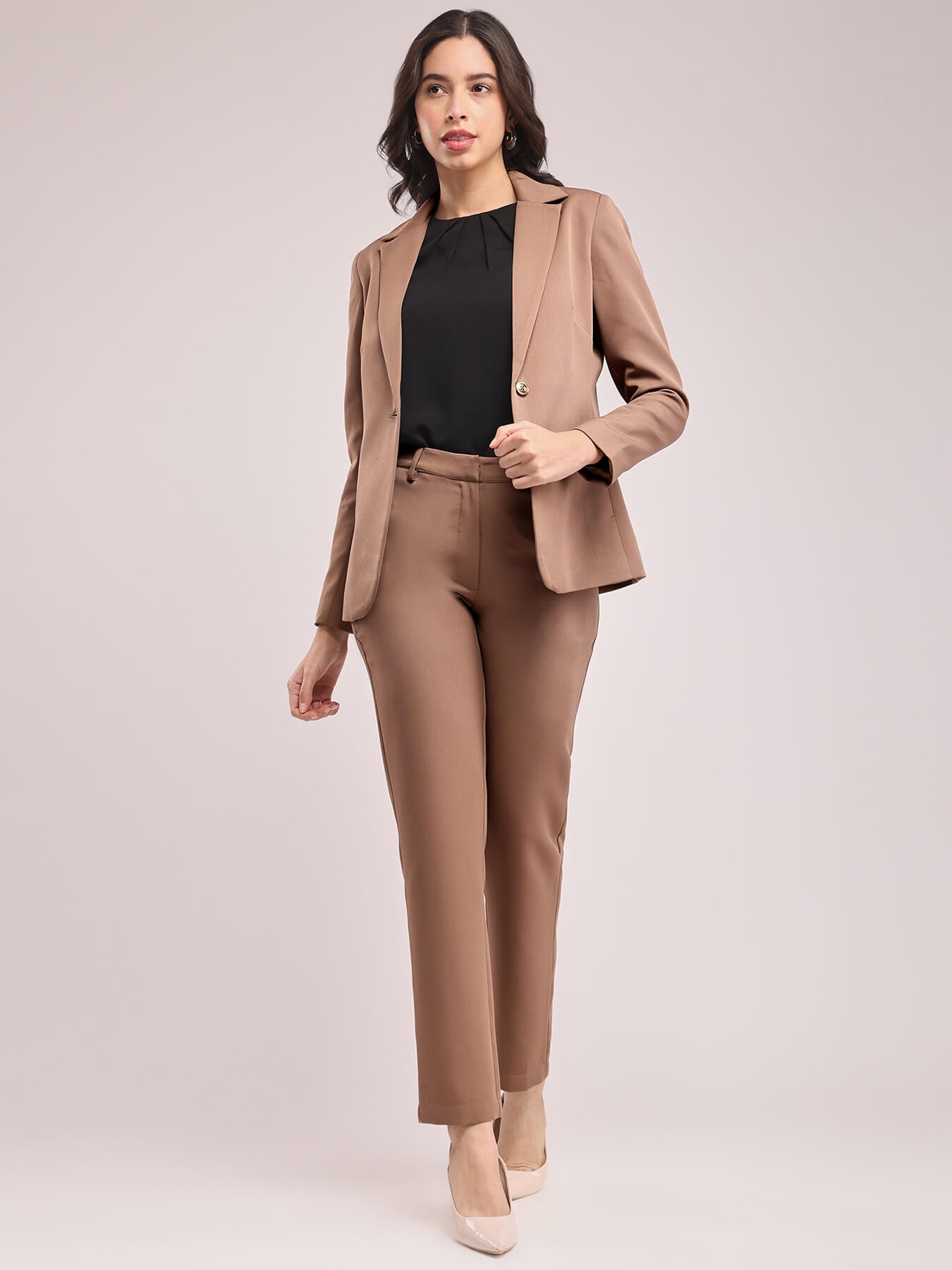 A woman modeling a brown single-breasted blazer and matching trousers, posing against a plain background. FableStreet