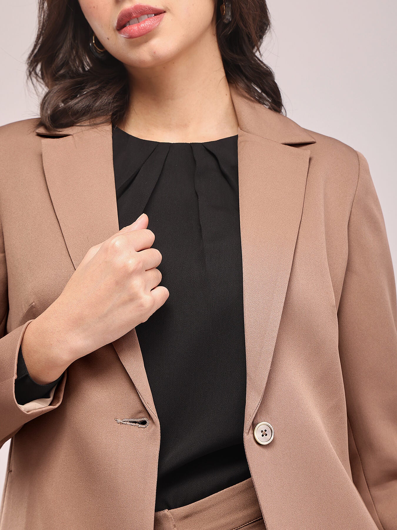 A woman modeling a brown single-breasted blazer and matching trousers, posing against a plain background. FableStreet