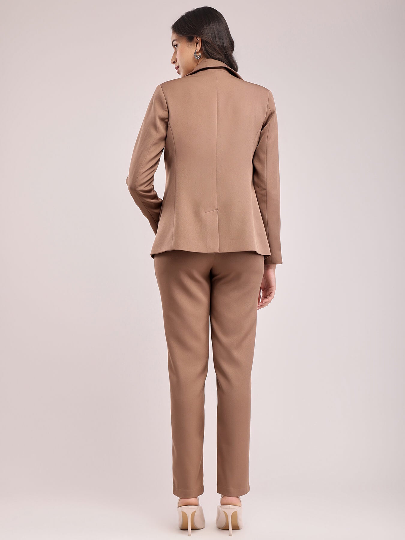 A woman modeling a brown single-breasted blazer and matching trousers, posing against a plain background. FableStreet