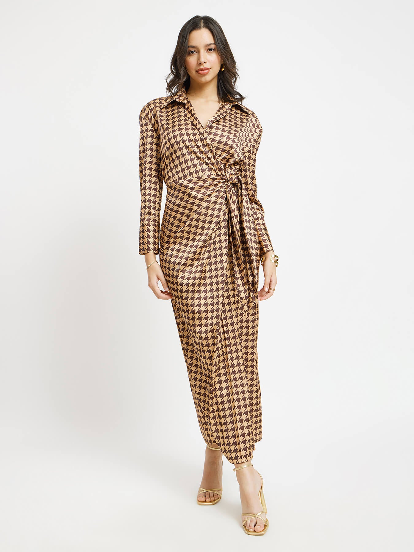 A model wearing a brown and gold houndstooth print satin wrap dress with a shirt collar and long sleeves.