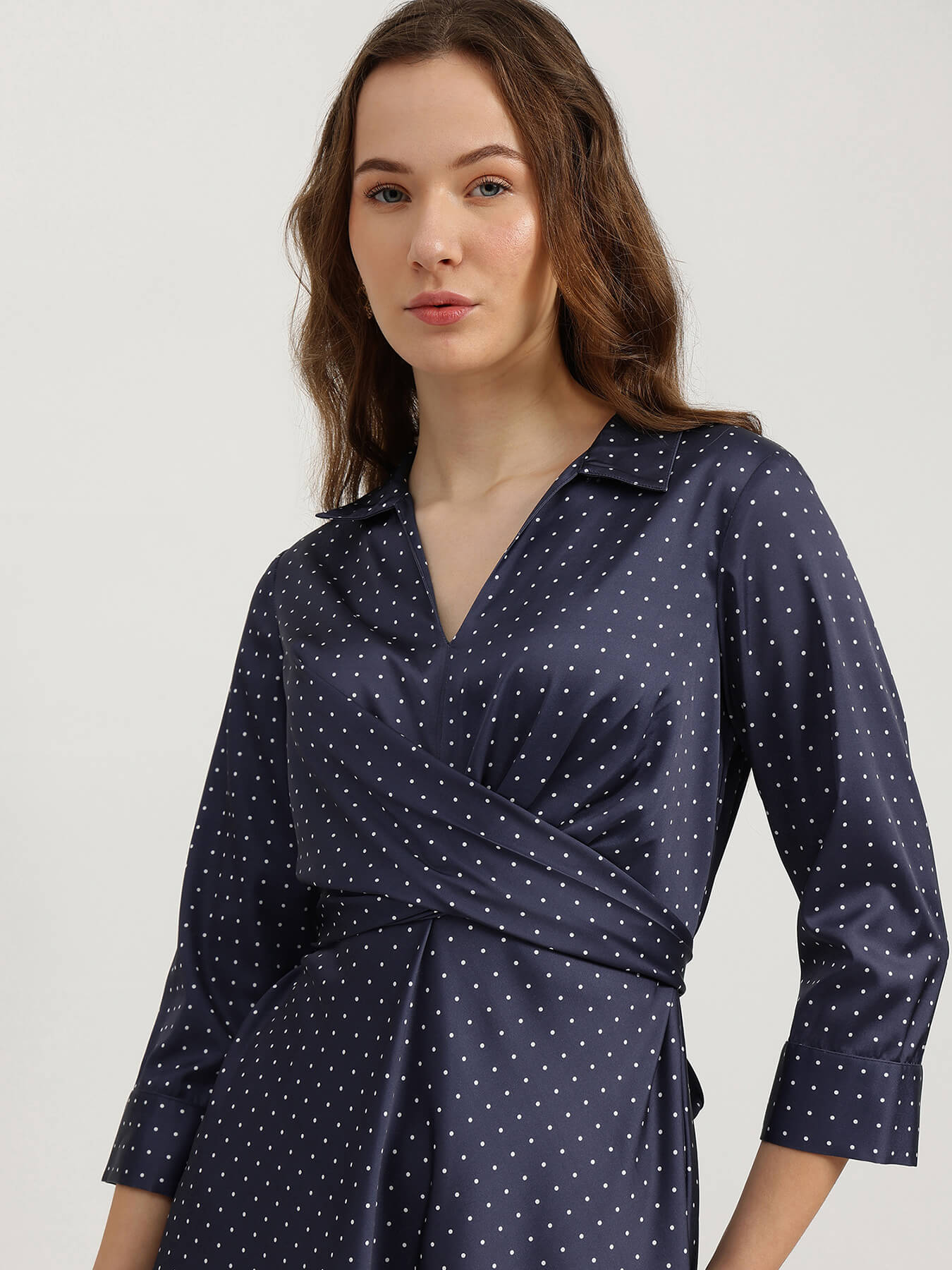 Woman wearing a navy blue dress with white polka dots on a light gray background