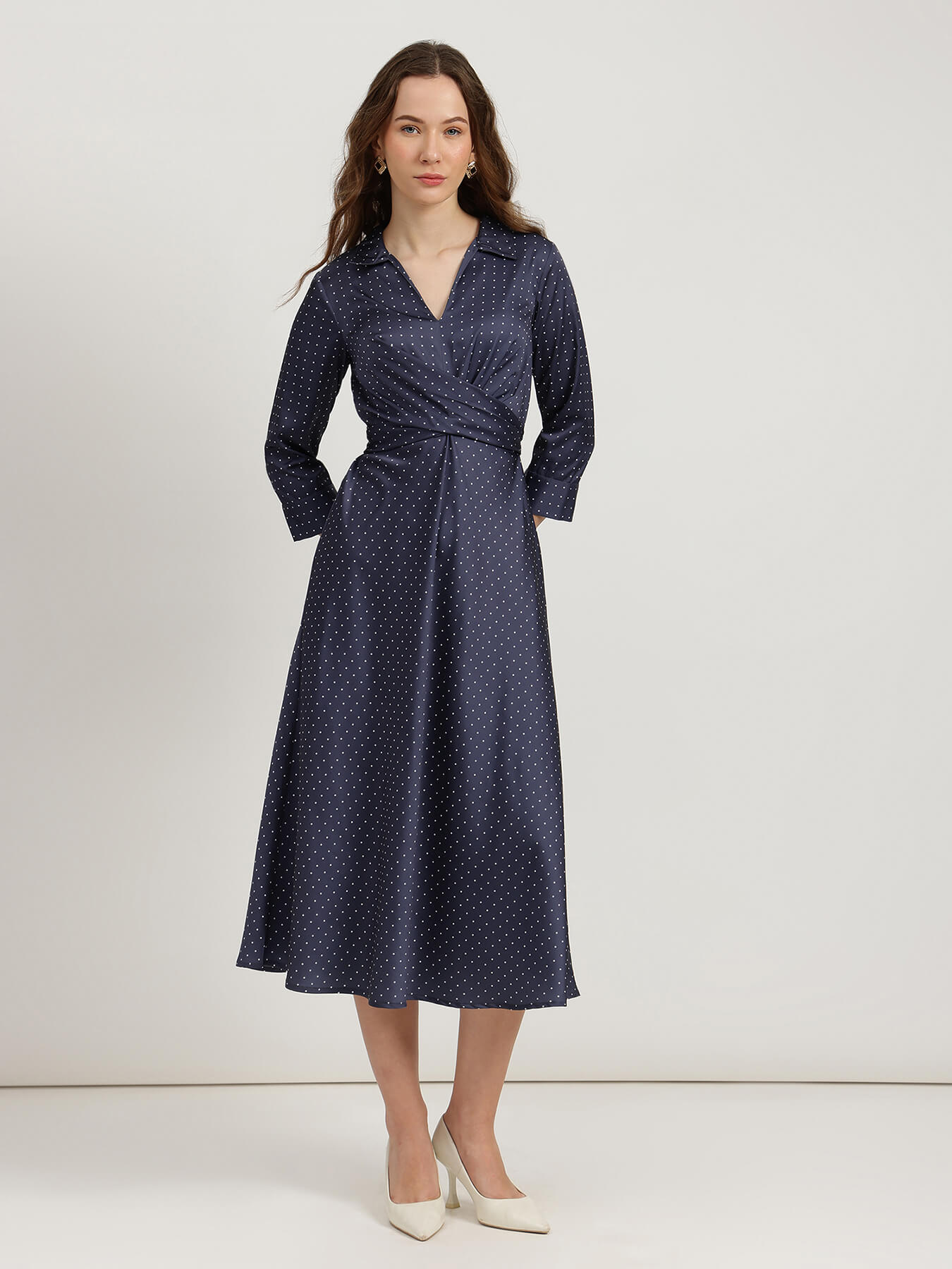Woman wearing a navy blue dress with white polka dots on a white background