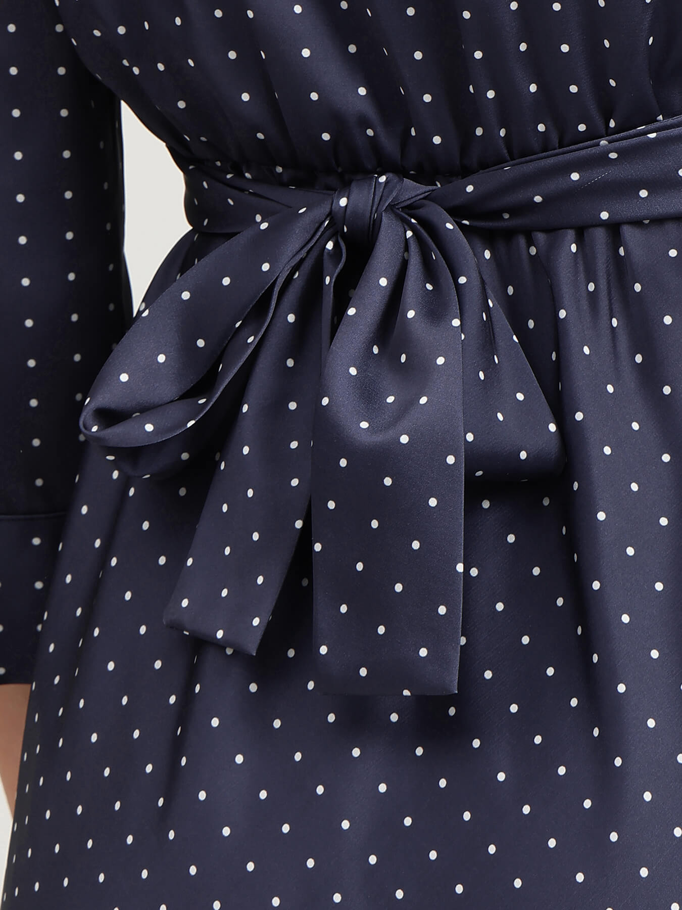 Navy blue dress with white polka dots and a tied belt on a plain background