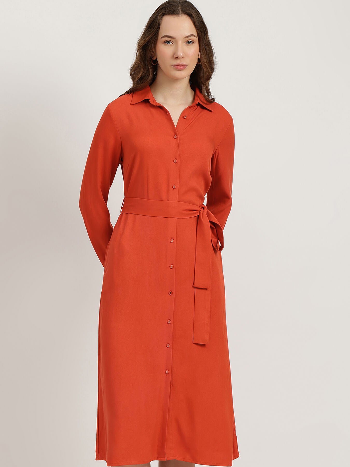 Woman wearing an orange dress with a belt on a light gray background