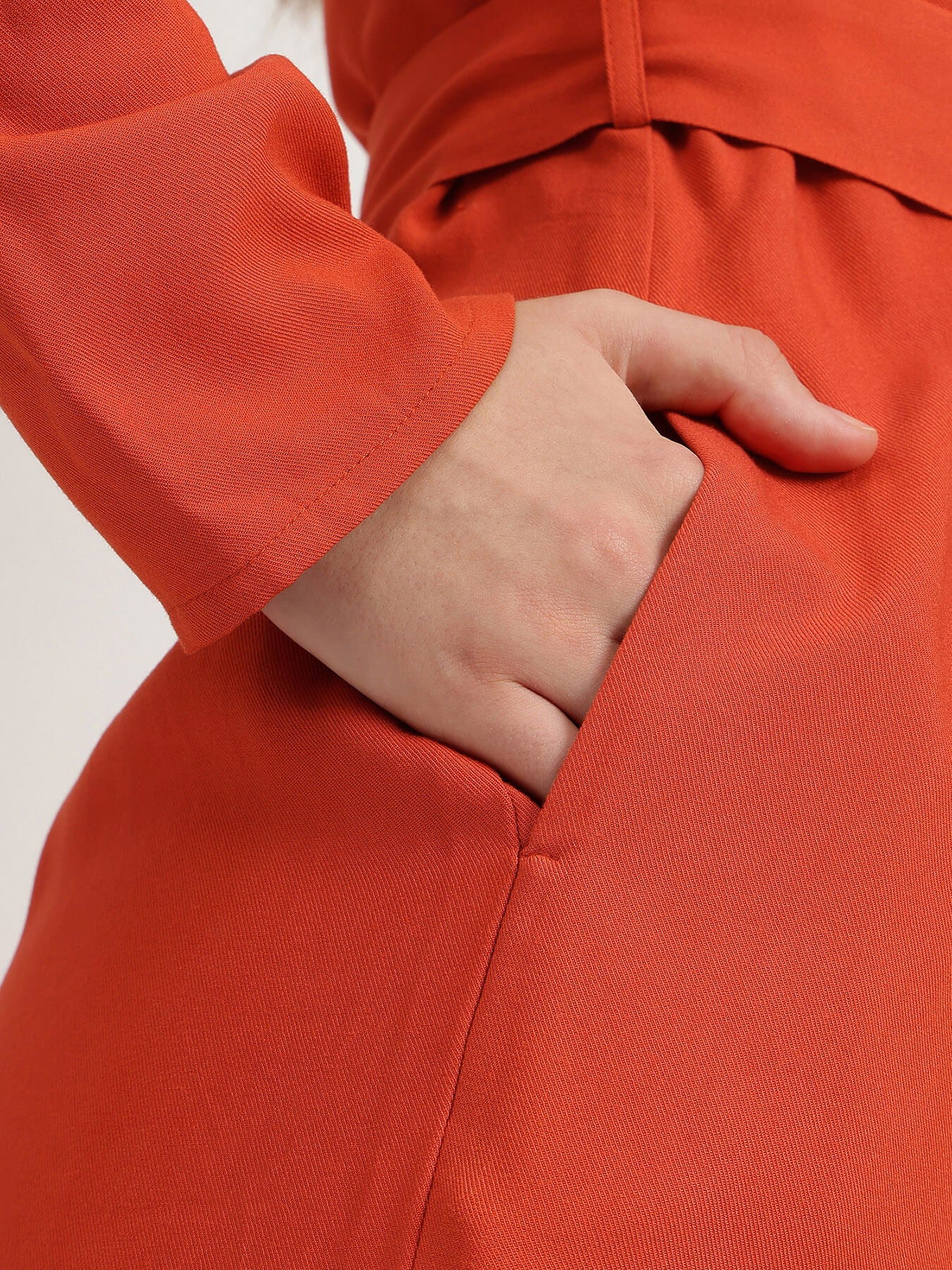 Person wearing an orange outfit with a hand in the pocket against a light background
