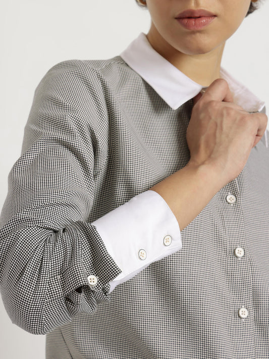 Close-up of a person wearing a checkered shirt with rolled-up sleeves and a white collar.