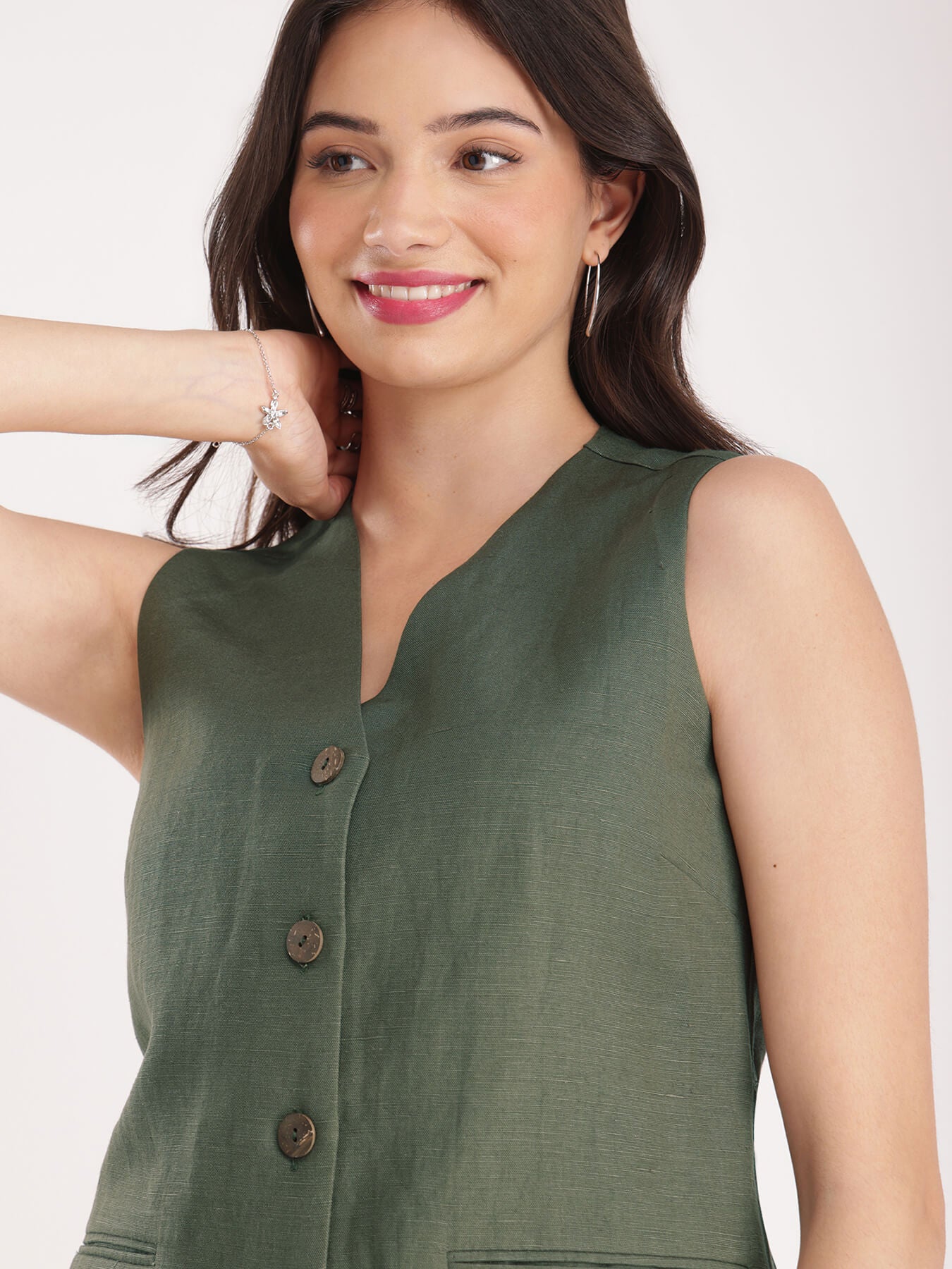 A woman wearing a green linen waistcoat with V-neck and 2 front pockets, paired with white trousers.