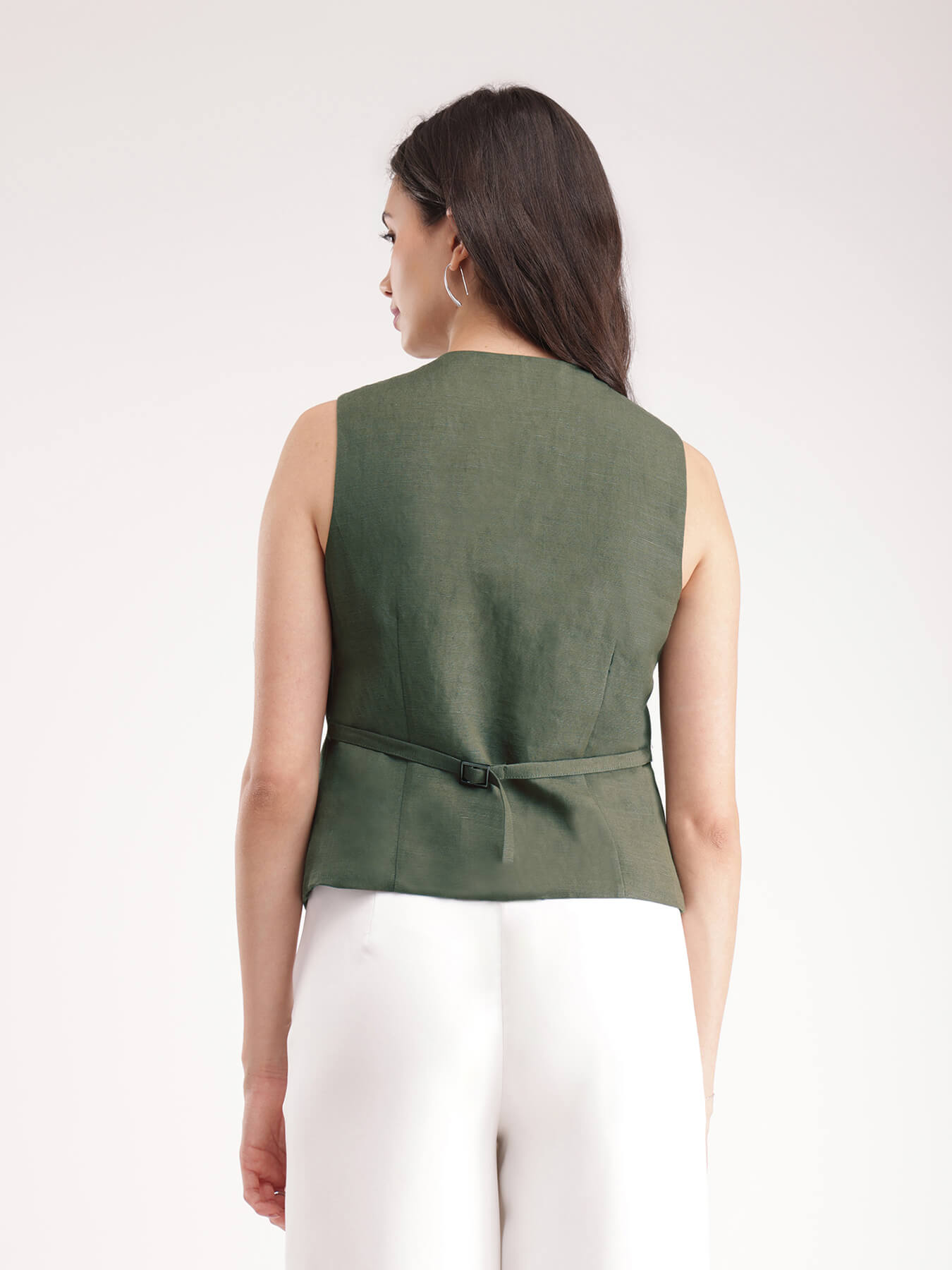 A woman wearing a green linen waistcoat with V-neck and 2 front pockets, paired with white trousers.