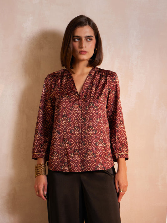 A woman wearing a maroon satin top with festive motif print, featuring a v-neck and three-quarter sleeves.