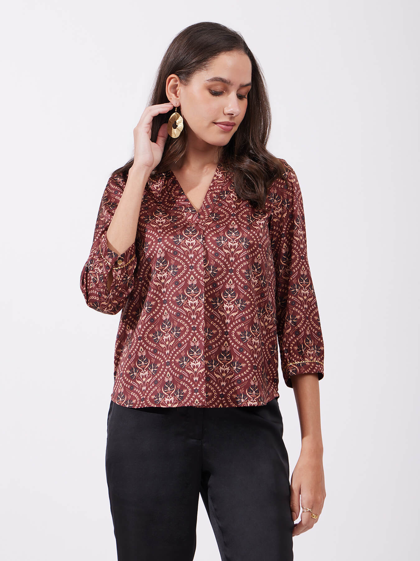 A woman wearing a maroon satin top with festive motif print, featuring a v-neck and three-quarter sleeves.