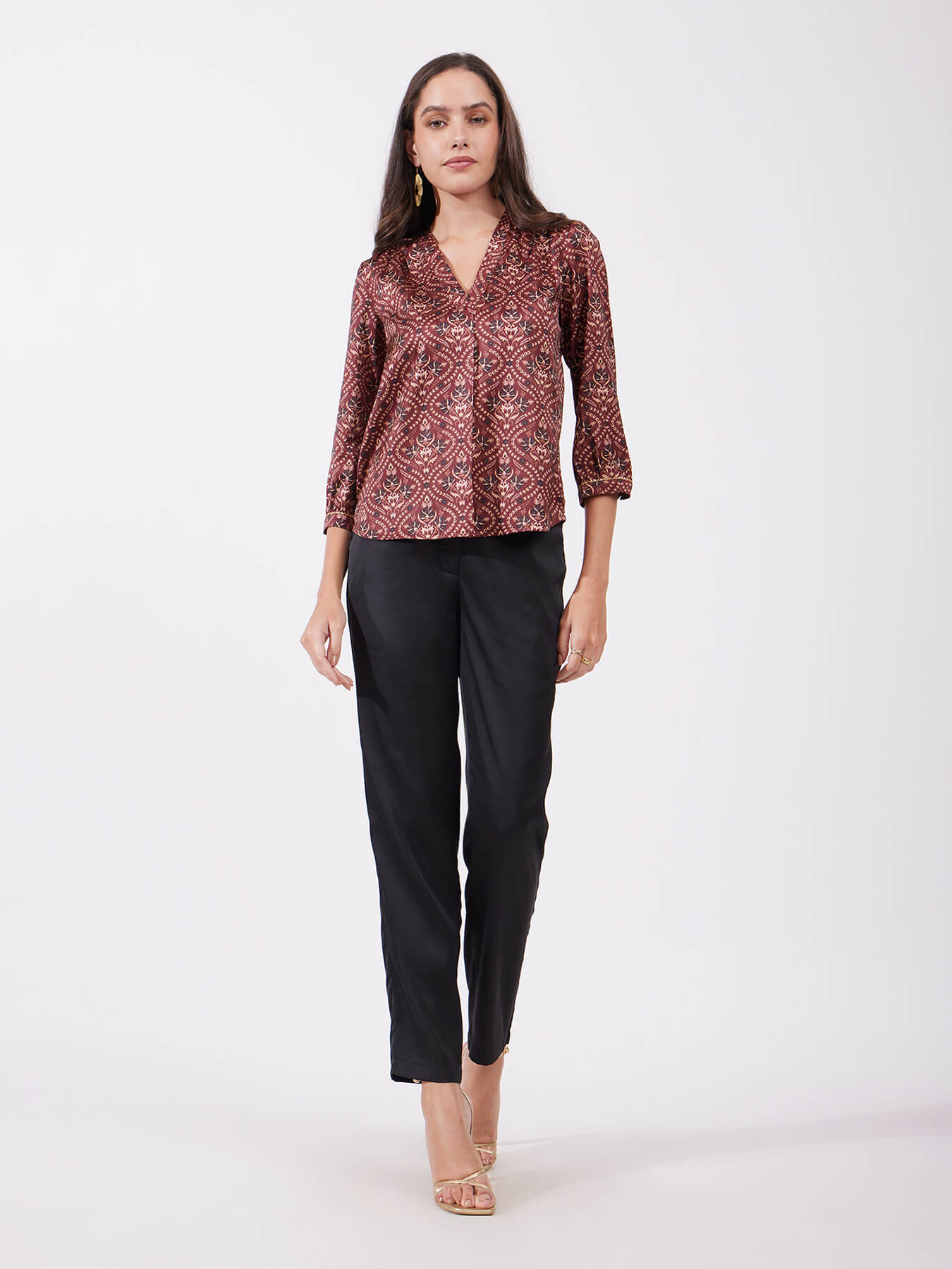 A woman wearing a maroon satin top with festive motif print, featuring a v-neck and three-quarter sleeves.