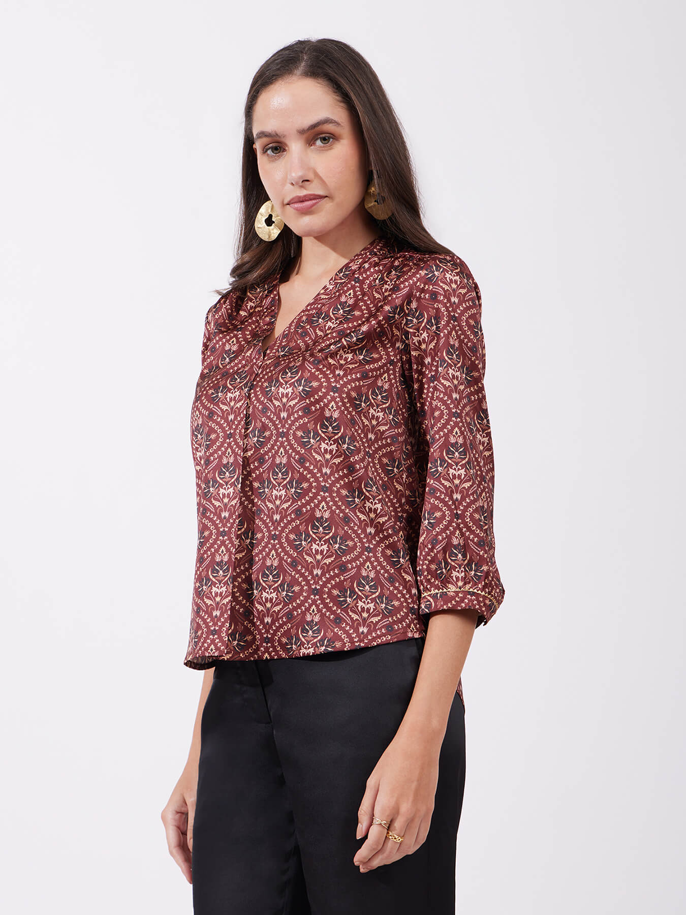 A woman wearing a maroon satin top with festive motif print, featuring a v-neck and three-quarter sleeves.