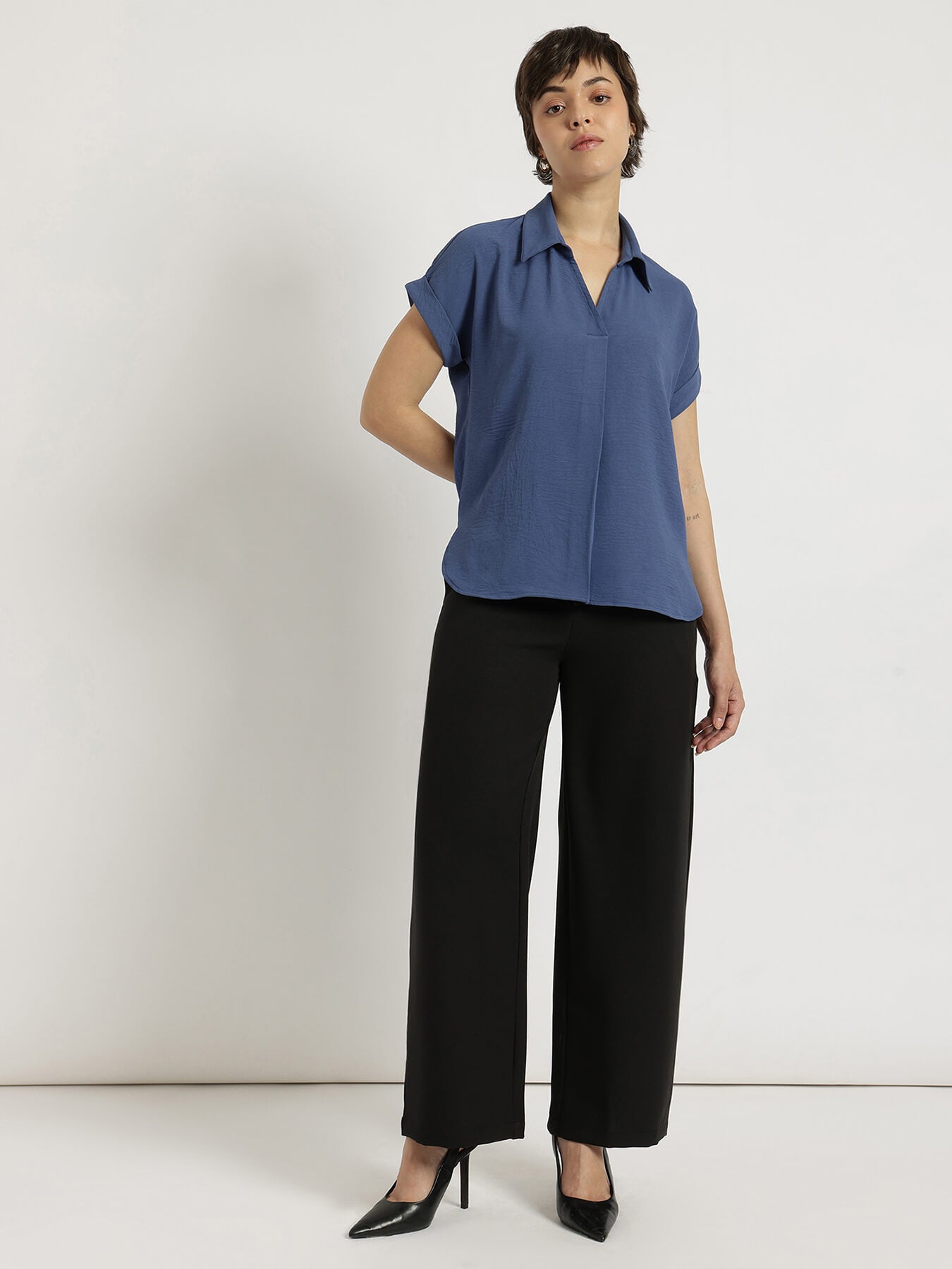 Woman wearing a blue blouse and black pants against a white background