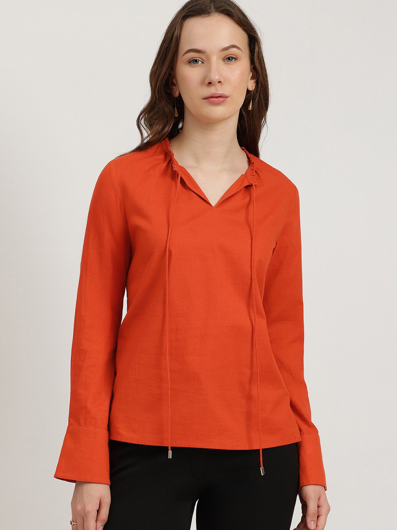 Woman wearing an orange long-sleeve shirt against a plain background
