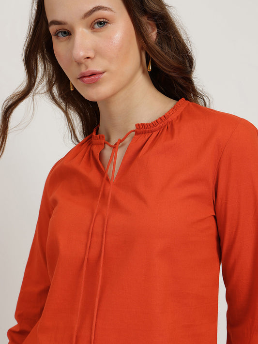 Woman wearing an orange blouse against a plain background