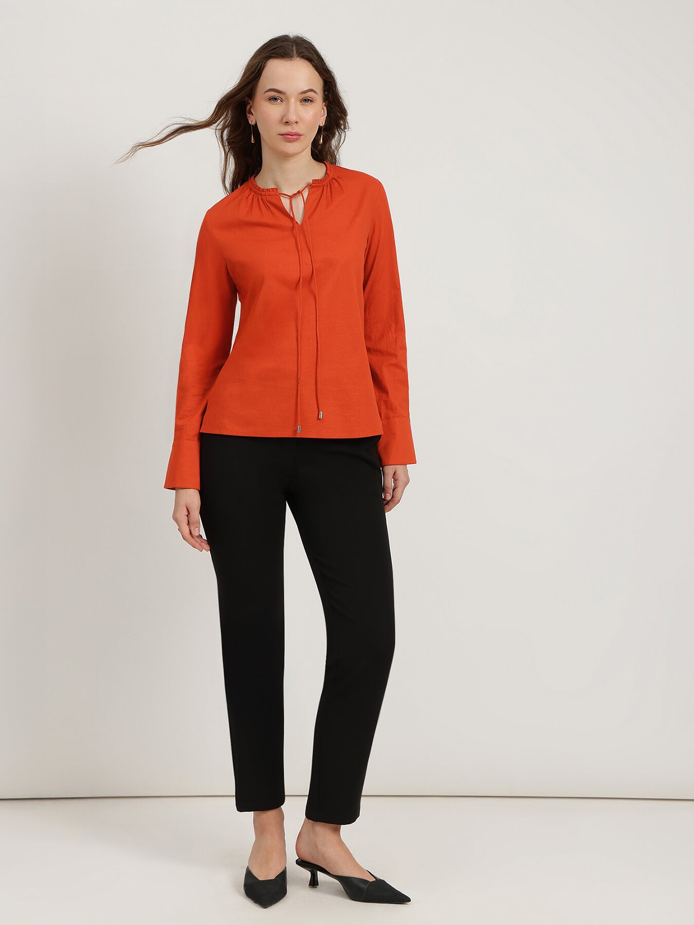 Woman wearing an orange blouse and black pants on a white background