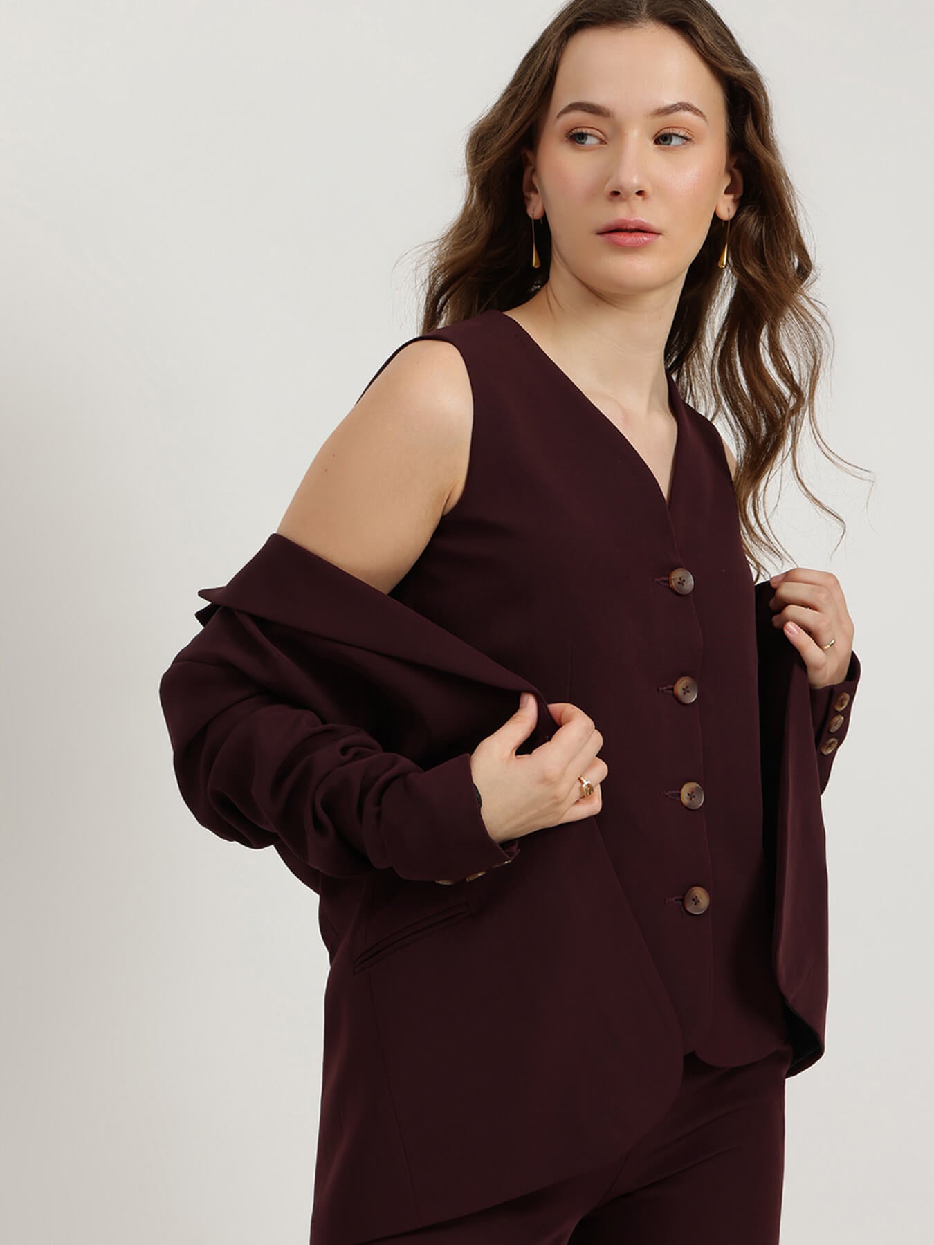 Woman wearing a burgundy outfit with a buttoned top on a plain background