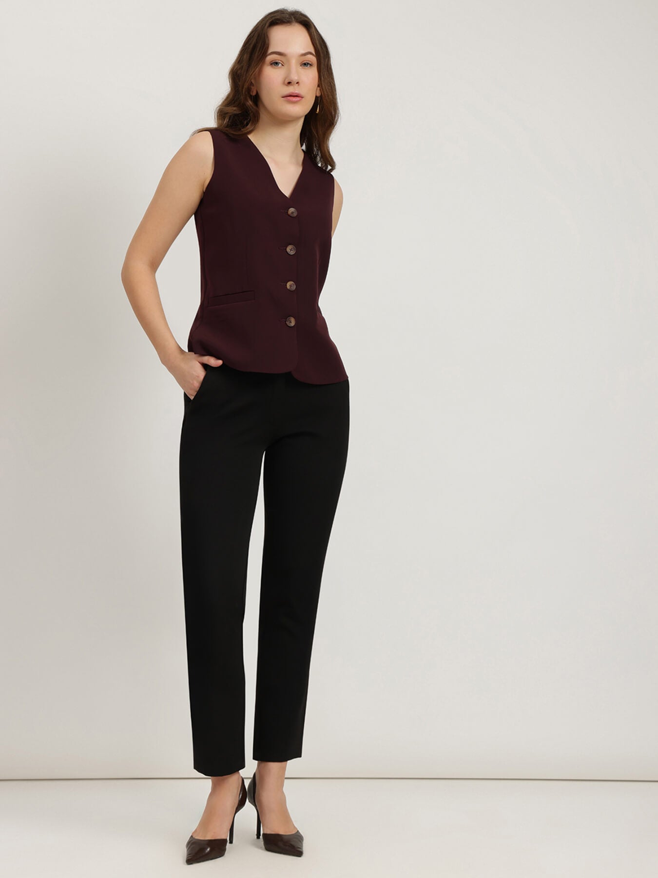 Woman wearing a sleeveless brown top with buttons and black pants on a white background