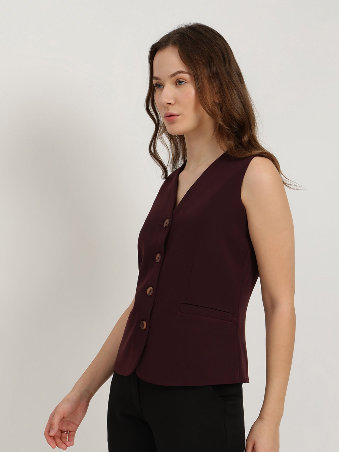 Woman wearing a burgundy sleeveless blazer against a plain background