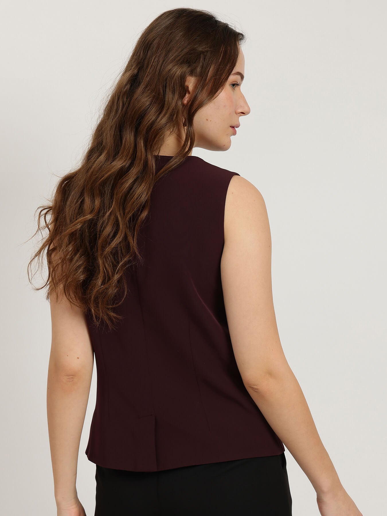 Woman wearing a sleeveless burgundy top against a plain background