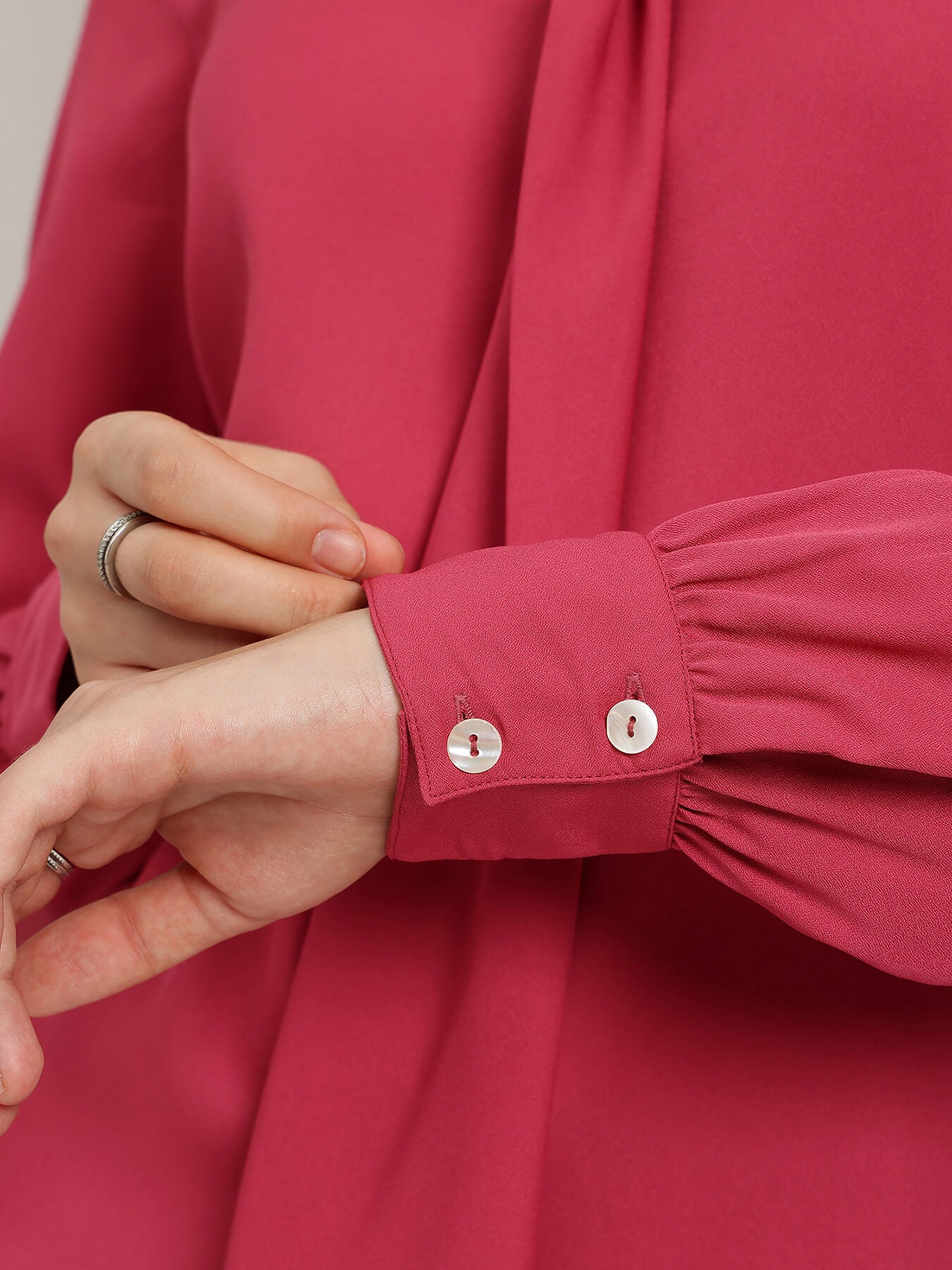Close-up of a person adjusting the cuff of a red shirt with a neutral background