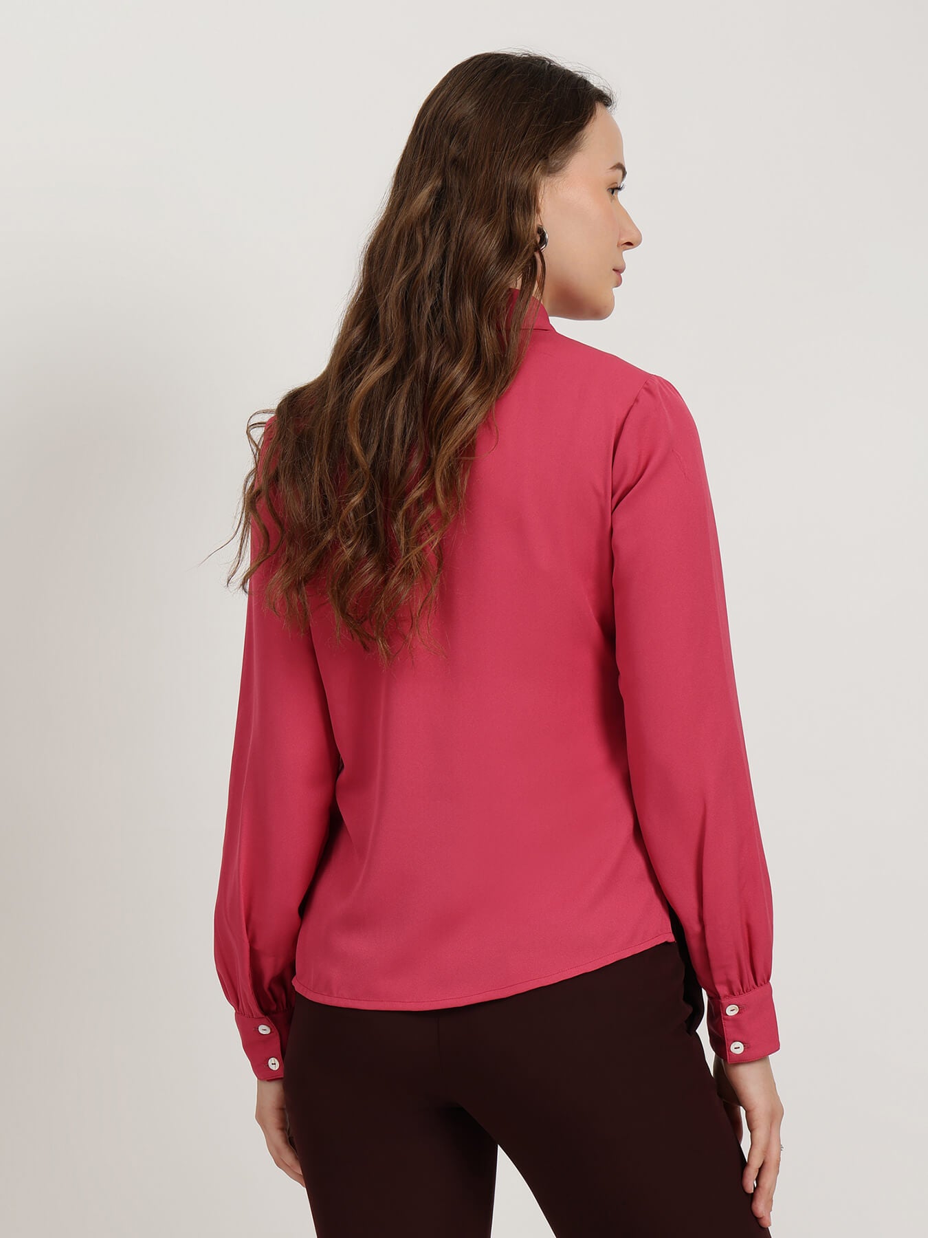 Woman wearing a pink blouse with long sleeves on a plain background