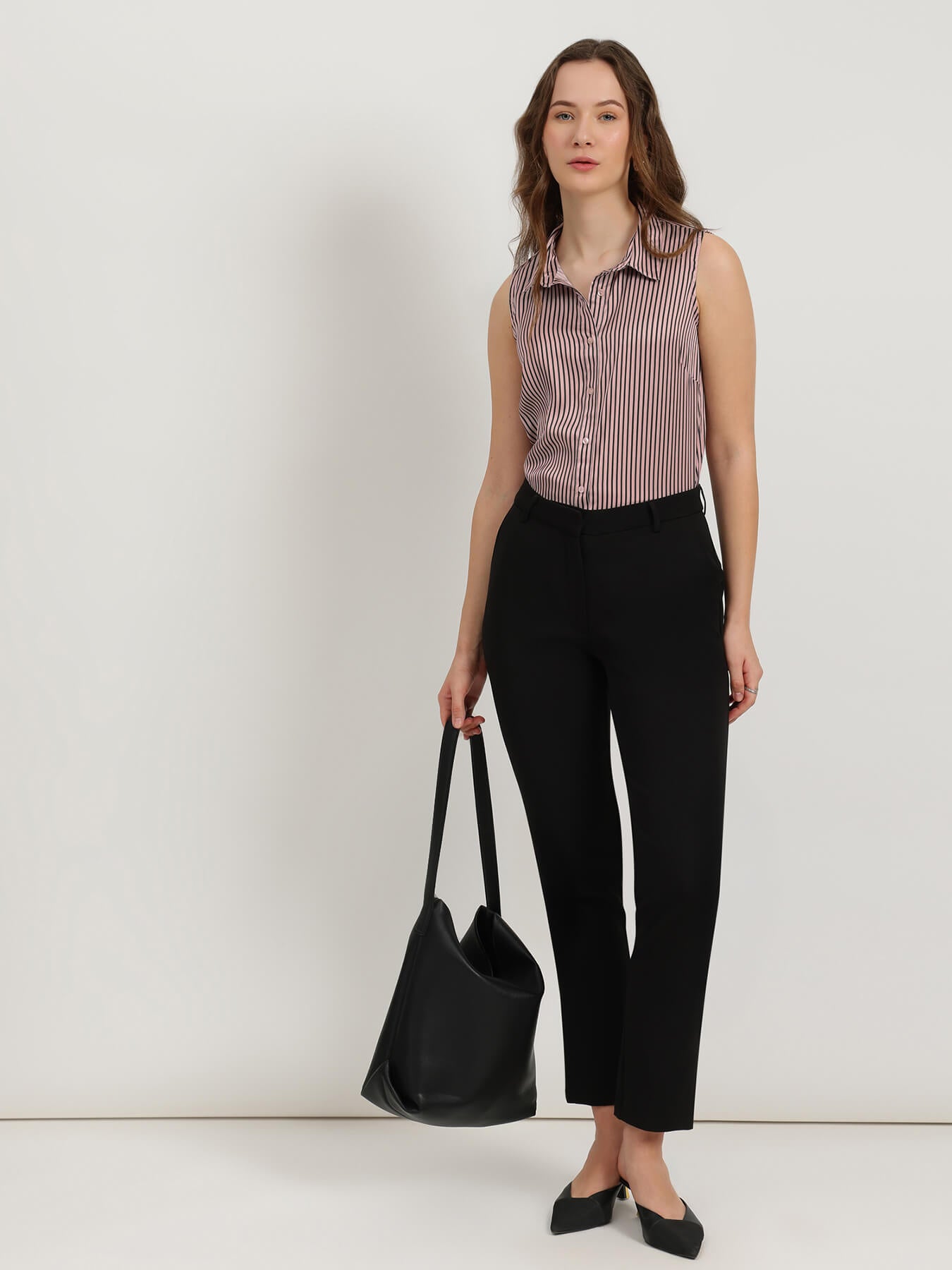 Woman wearing a striped shirt and black pants, holding a black bag against a white background