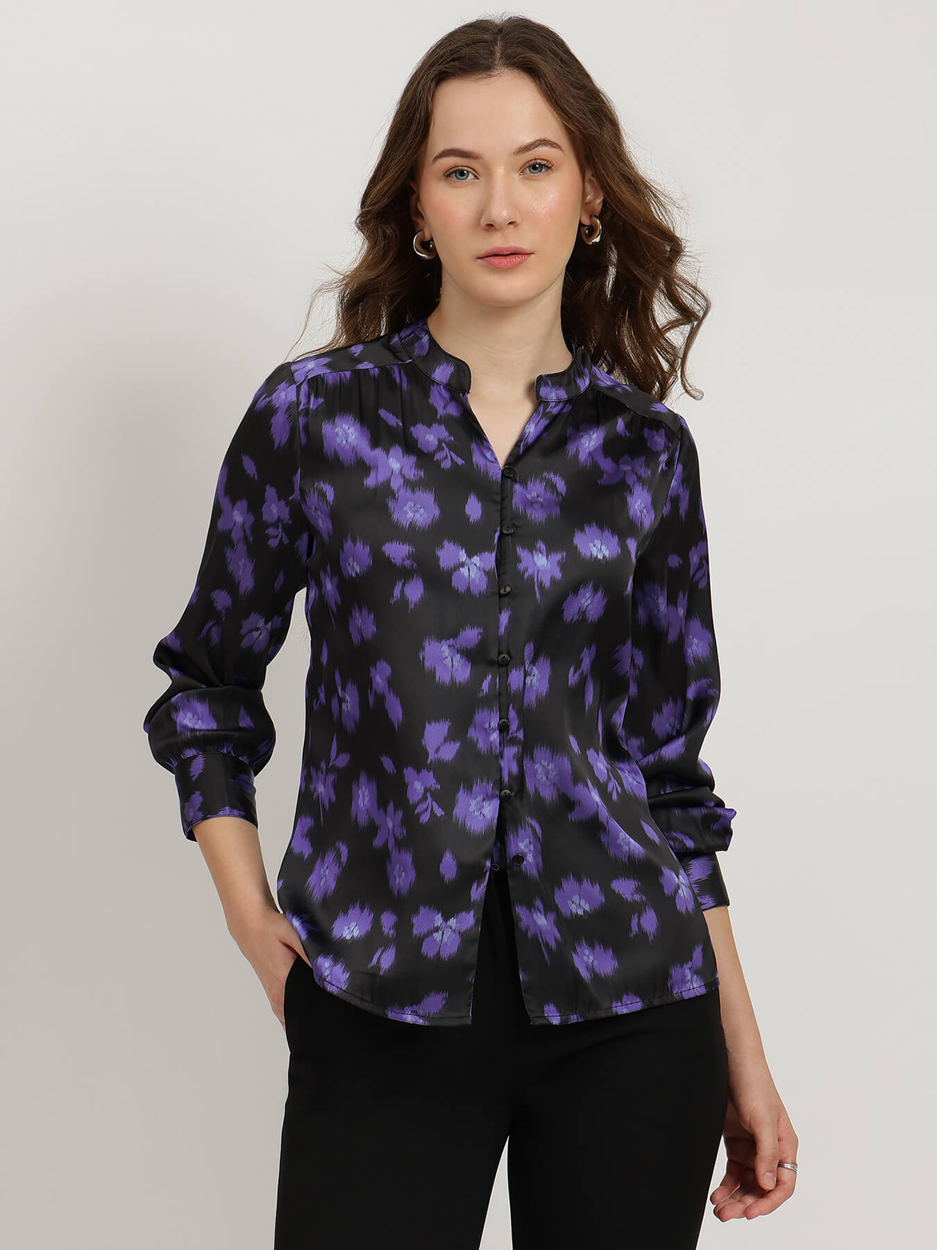 Woman wearing a black shirt with purple floral pattern against a plain background