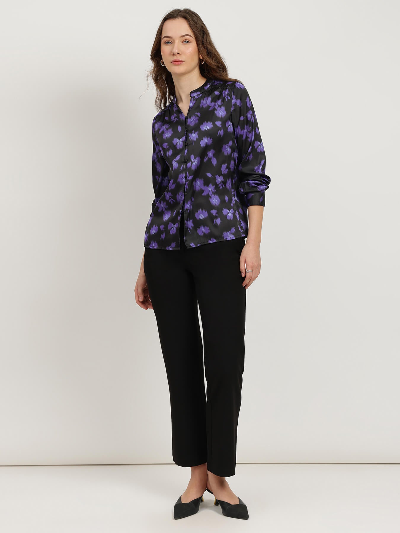 Woman wearing a black and purple floral blouse with black pants on a white background