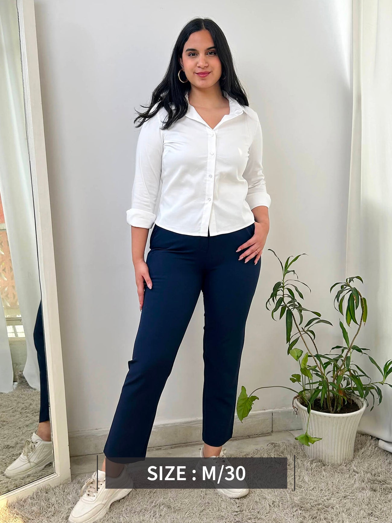 A person standing wearing navy blue straight fit trousers with pockets, paired with a white top and light-colored shoes.