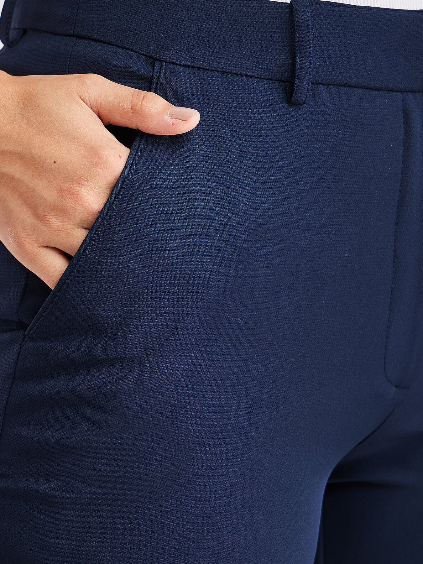 A person standing wearing navy blue straight fit trousers with pockets, paired with a white top and light-colored shoes.