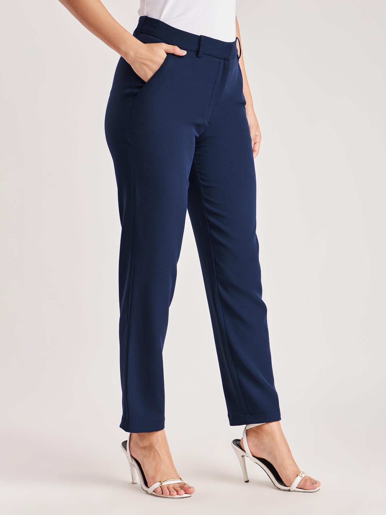 A person standing wearing navy blue straight fit trousers with pockets, paired with a white top and light-colored shoes.
