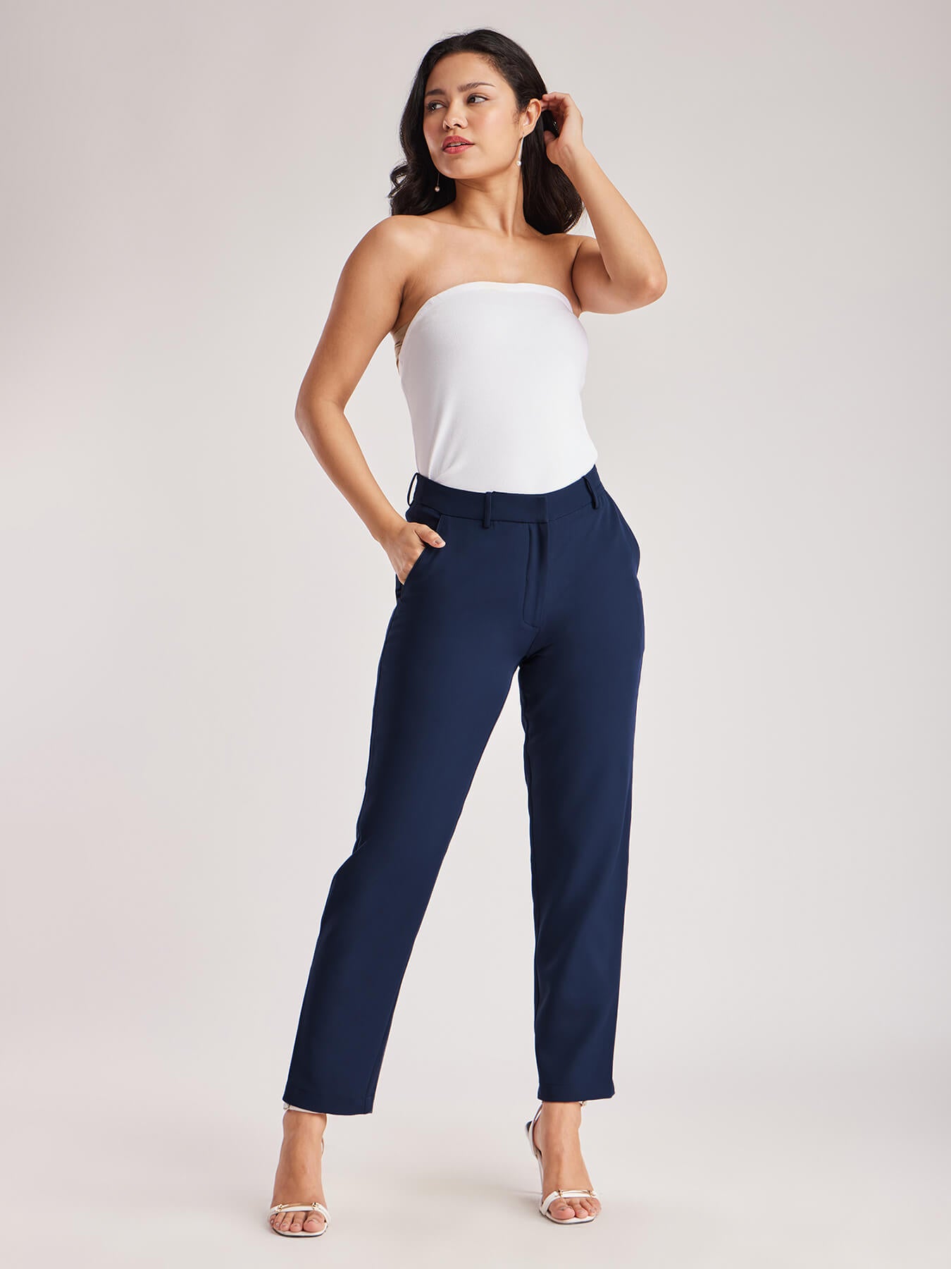 A person standing wearing navy blue straight fit trousers with pockets, paired with a white top and light-colored shoes.