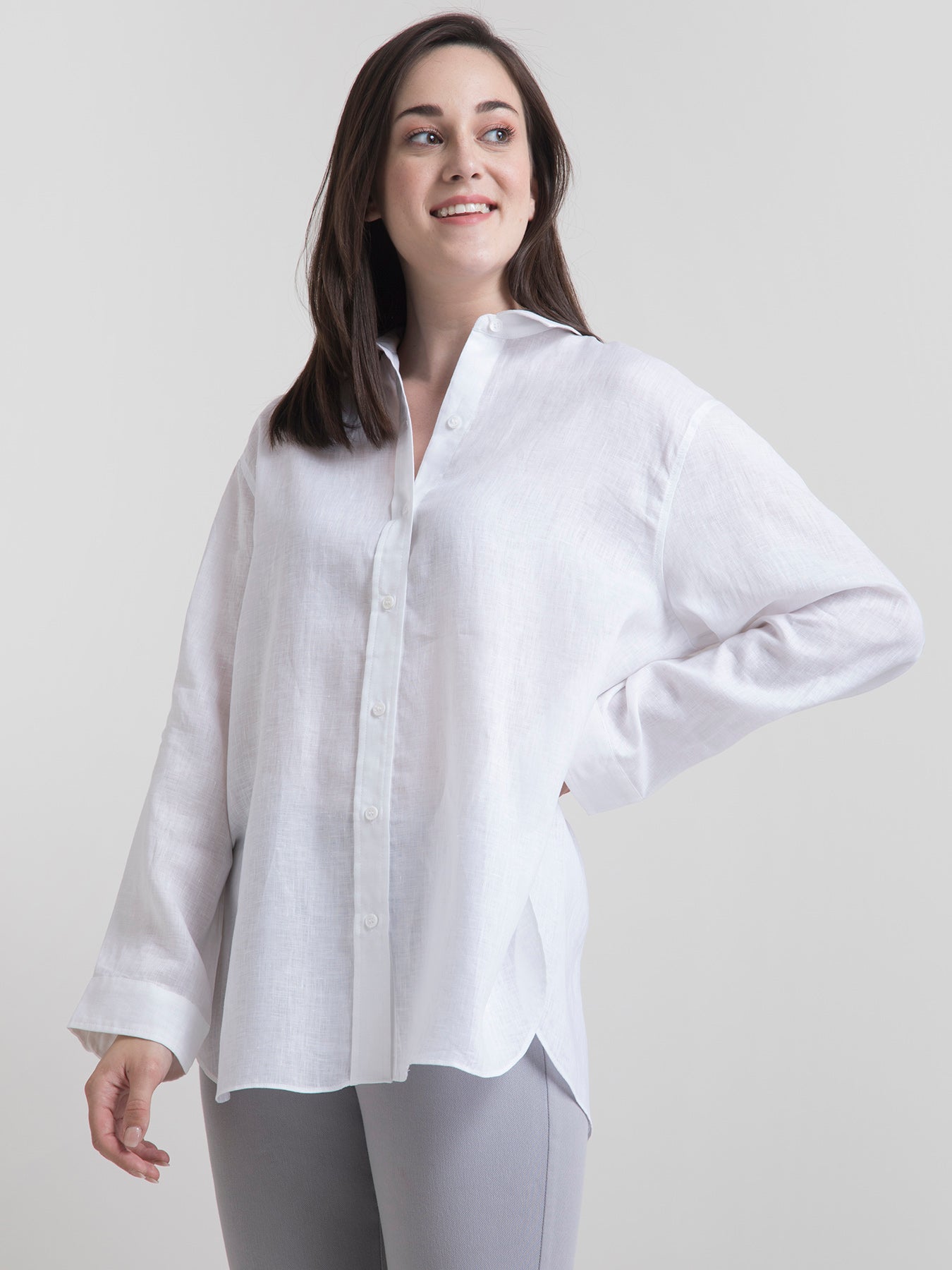 A woman smiling, wearing a white oversized collared shirt with long sleeves and a button placket.