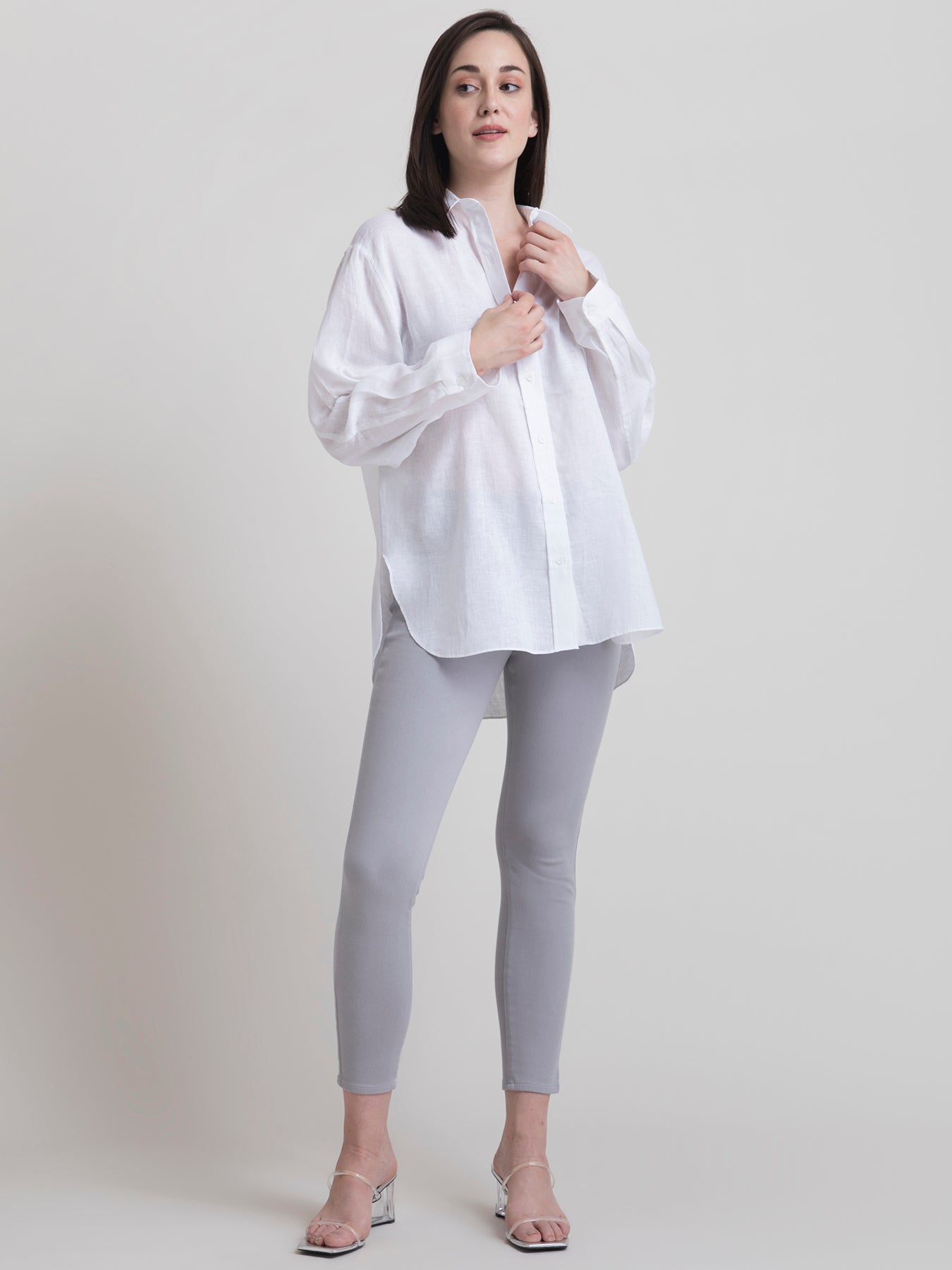A woman smiling, wearing a white oversized collared shirt with long sleeves and a button placket.