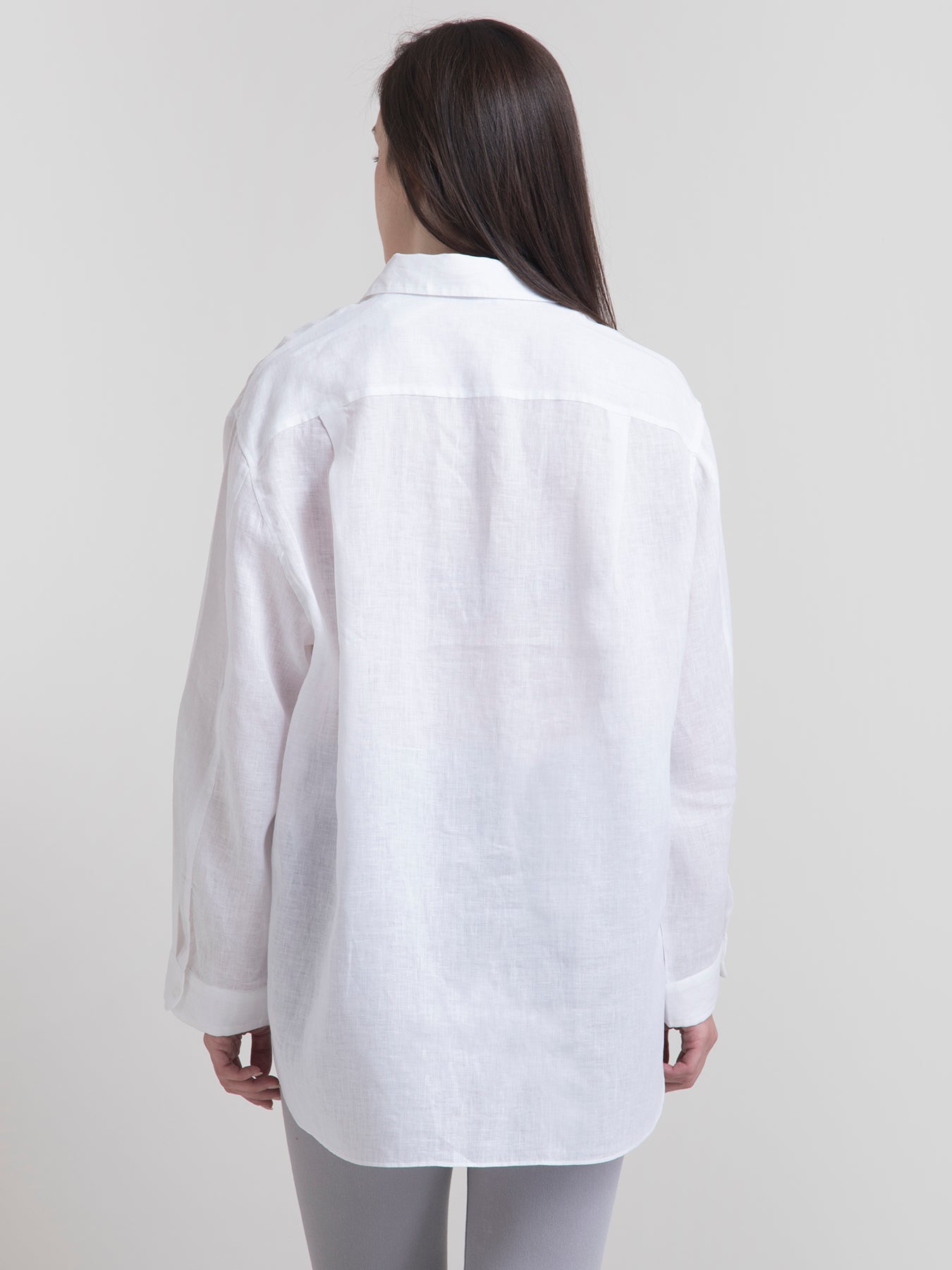 A woman smiling, wearing a white oversized collared shirt with long sleeves and a button placket.