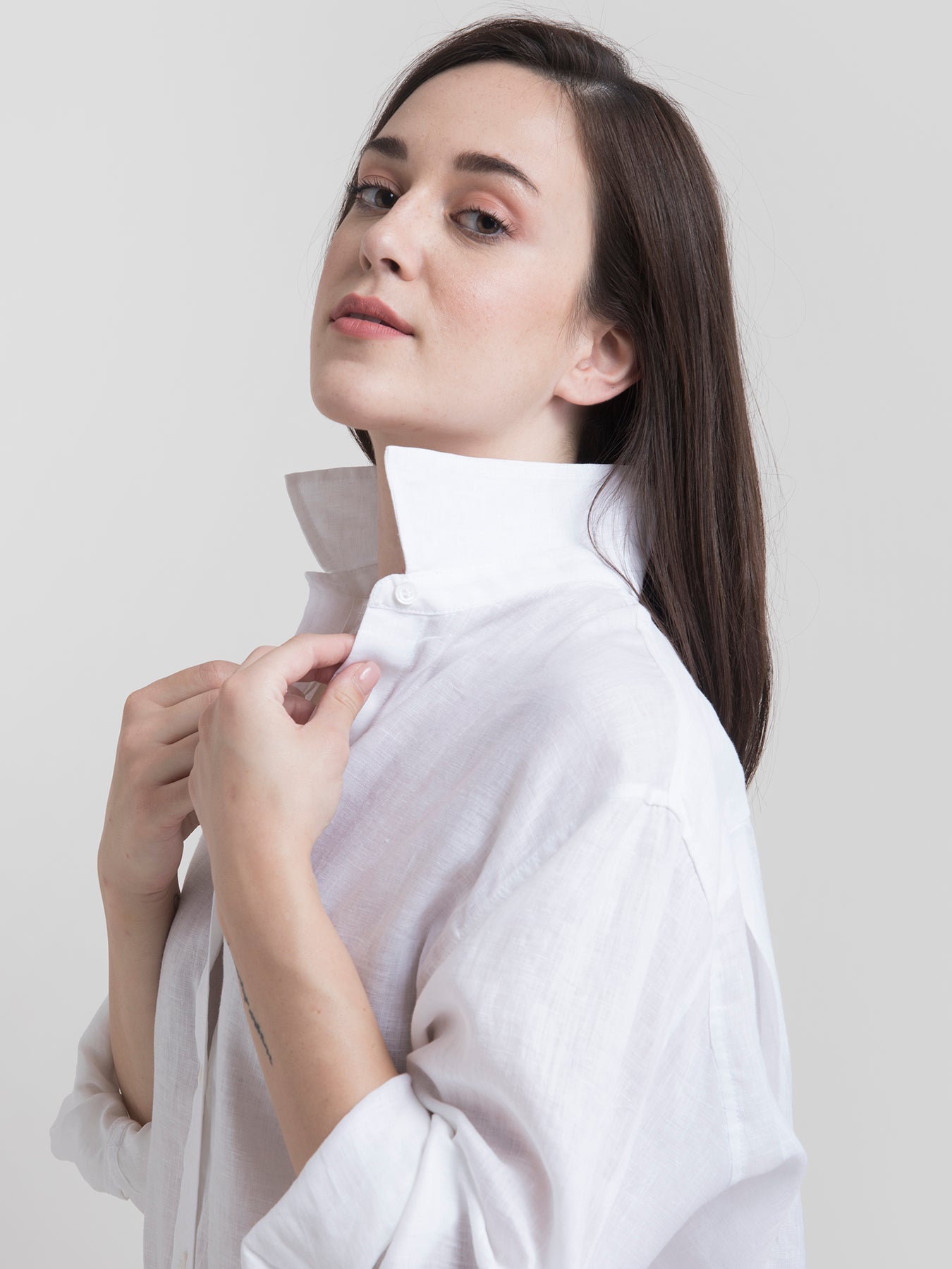 A woman smiling, wearing a white oversized collared shirt with long sleeves and a button placket.