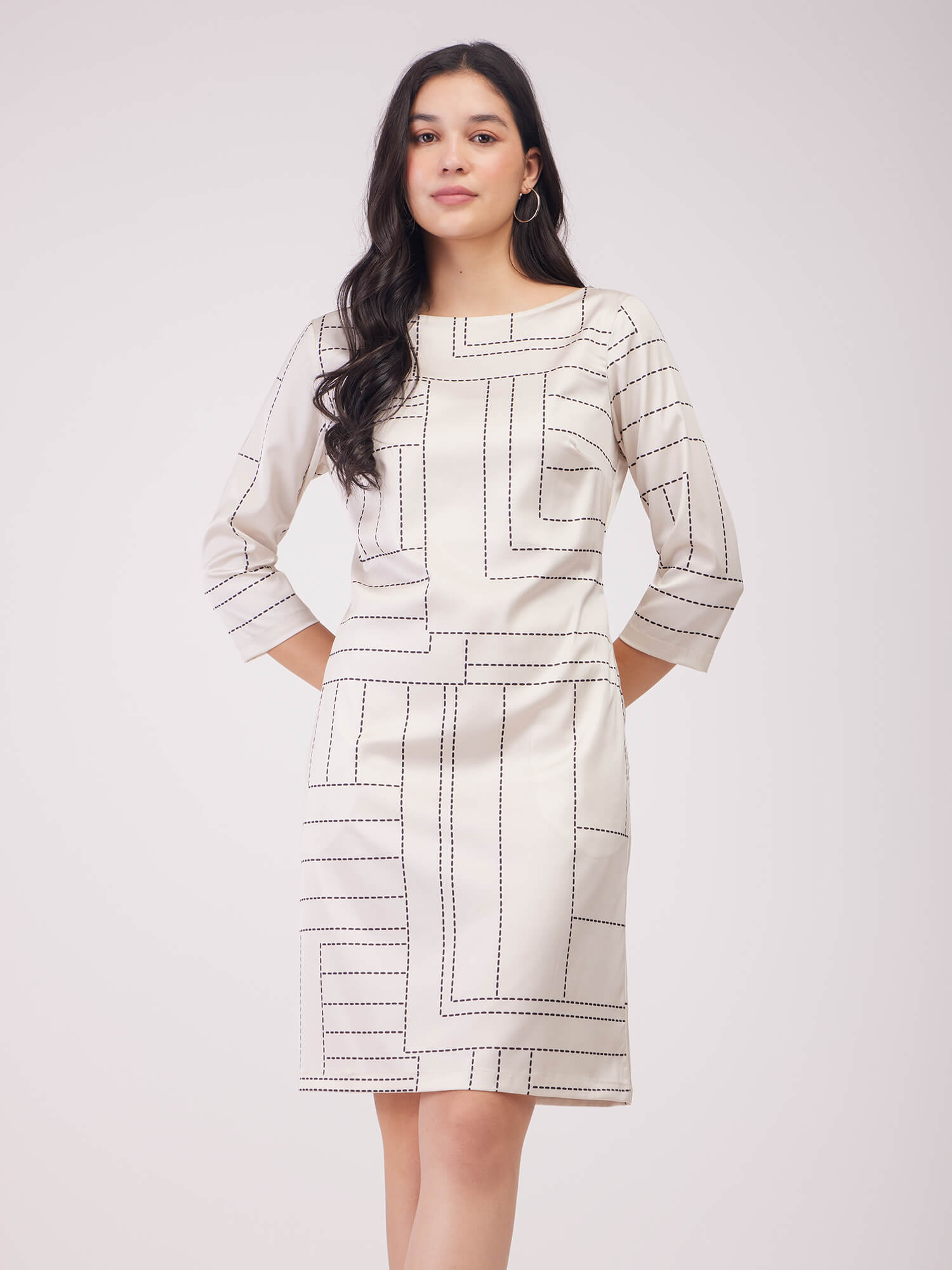 A woman wearing an off white geometric print shift dress with three-quarter sleeves, boat neck, and two pockets.
