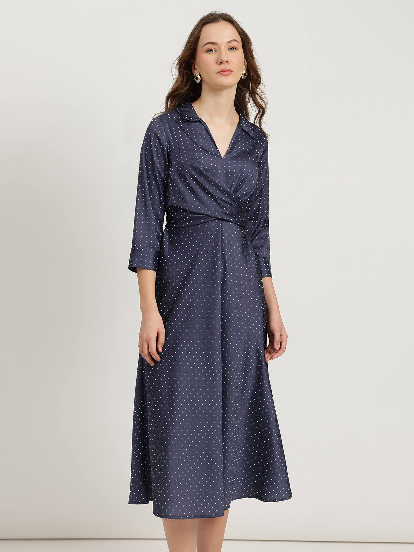 Woman wearing a navy blue dress with white polka dots on a white background