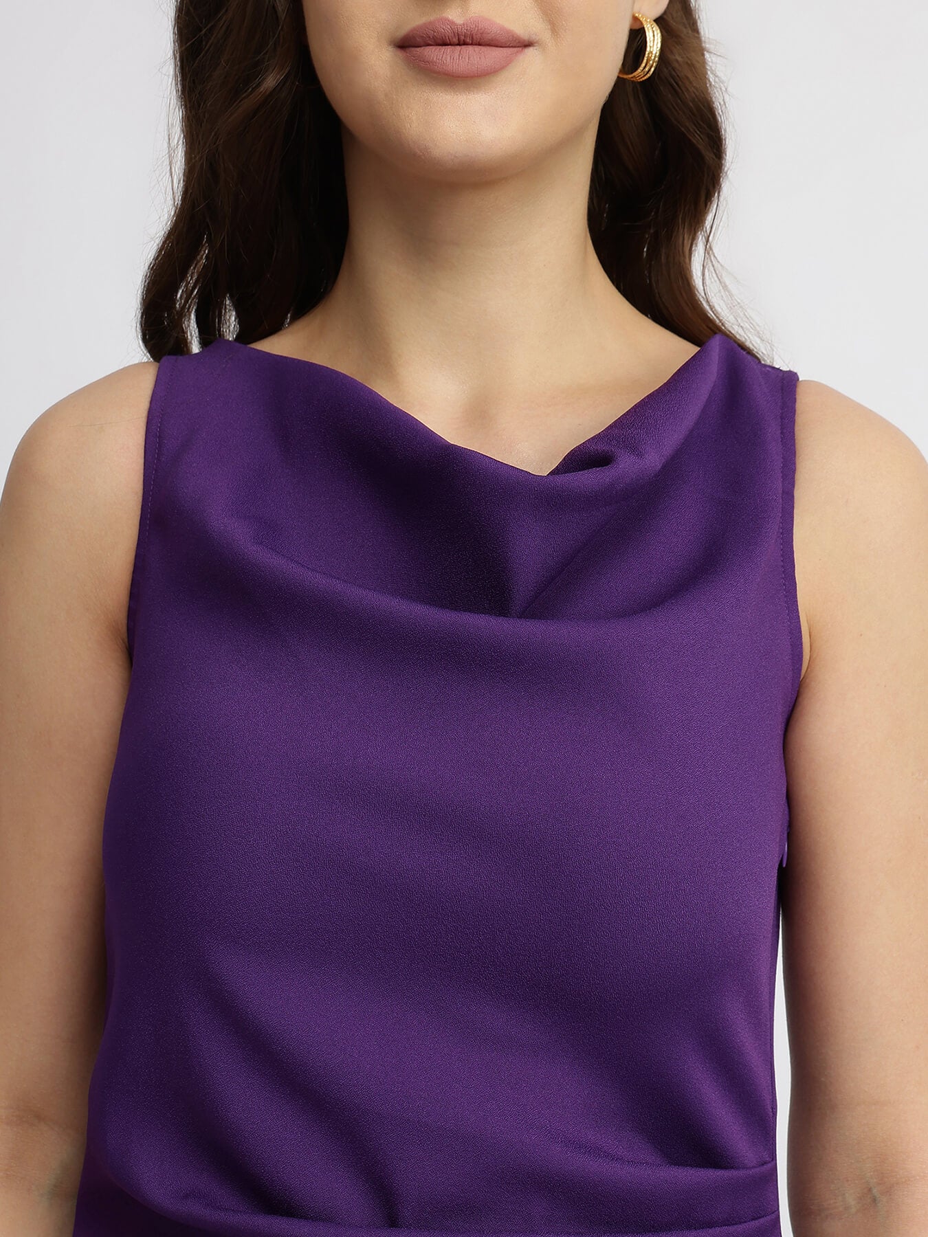 A woman modeling a purple pleated midi dress with a cowl neck and A-line silhouette.