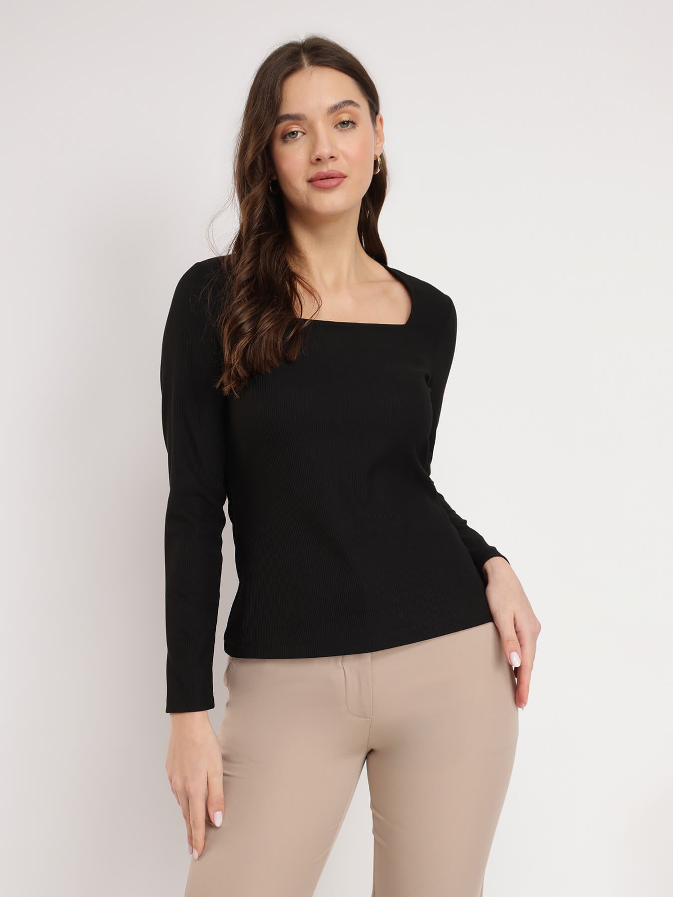 A woman wearing a black square neck top with long sleeves, paired with beige pants.