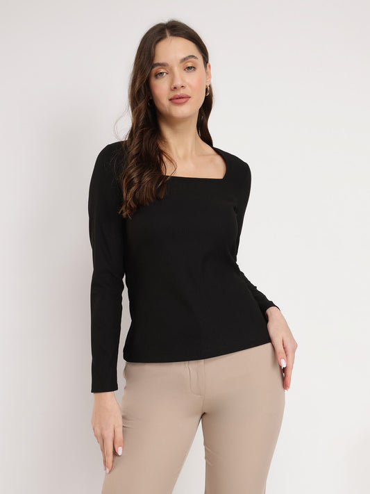 A woman wearing a black square neck top with long sleeves, paired with beige pants.
