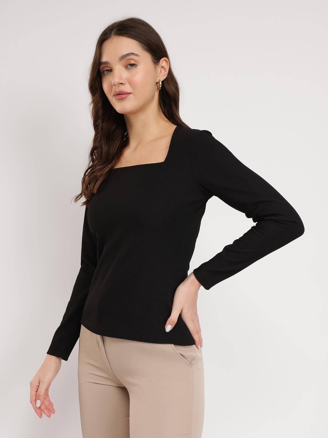 A woman wearing a black square neck top with long sleeves, paired with beige pants.