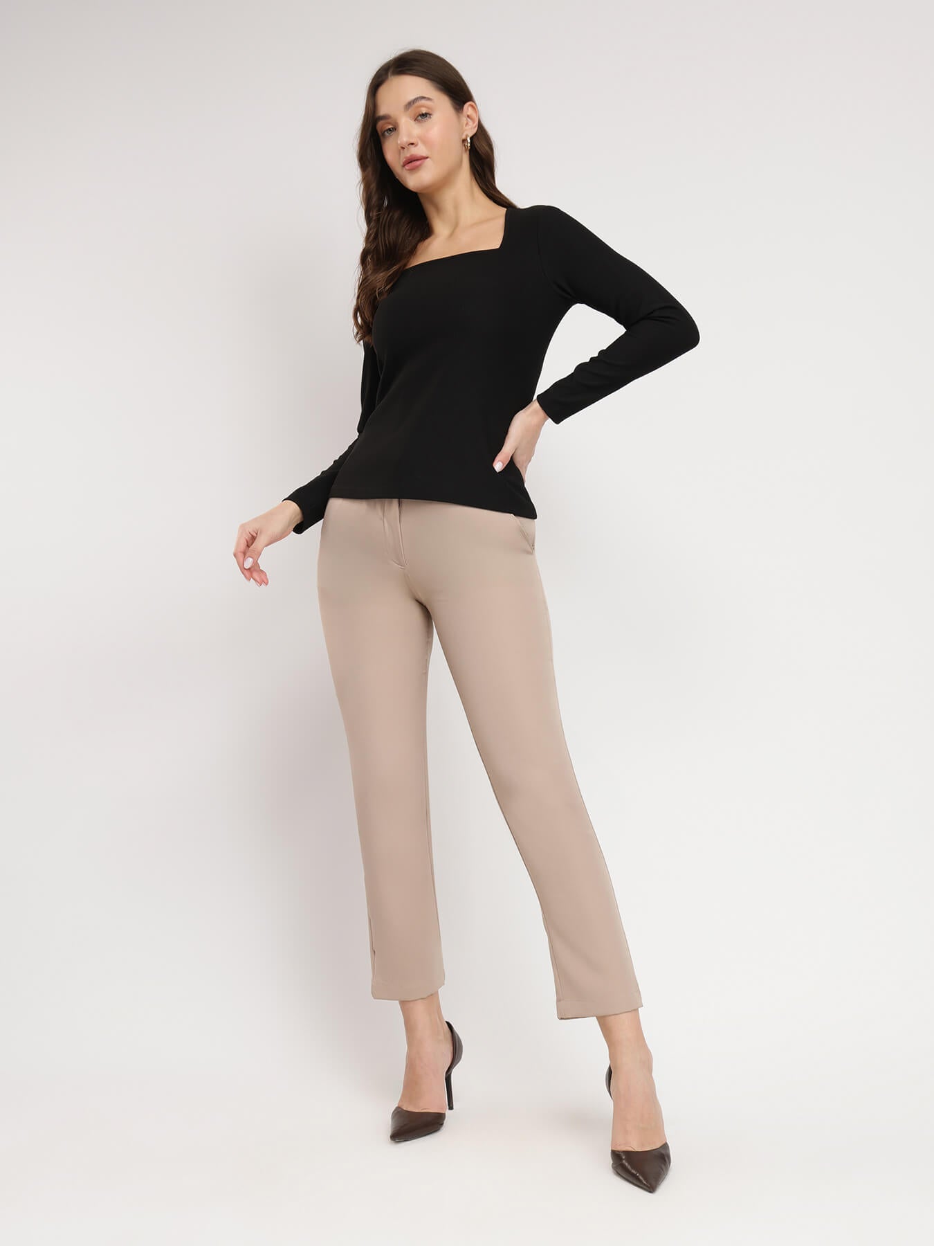 A woman wearing a black square neck top with long sleeves, paired with beige pants.