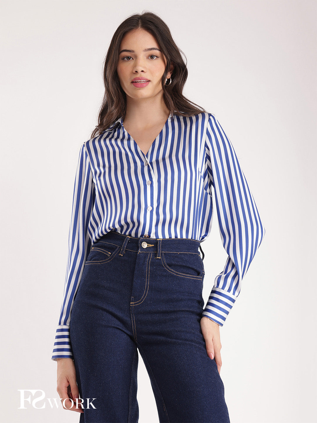 Woman wearing a blue and white striped shirt and dark jeans on a white background