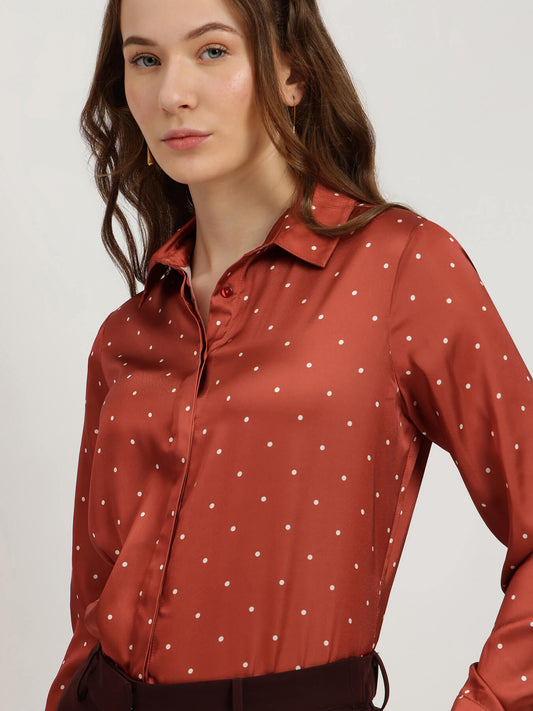 Woman wearing a rust-colored blouse with white polka dots on a plain background