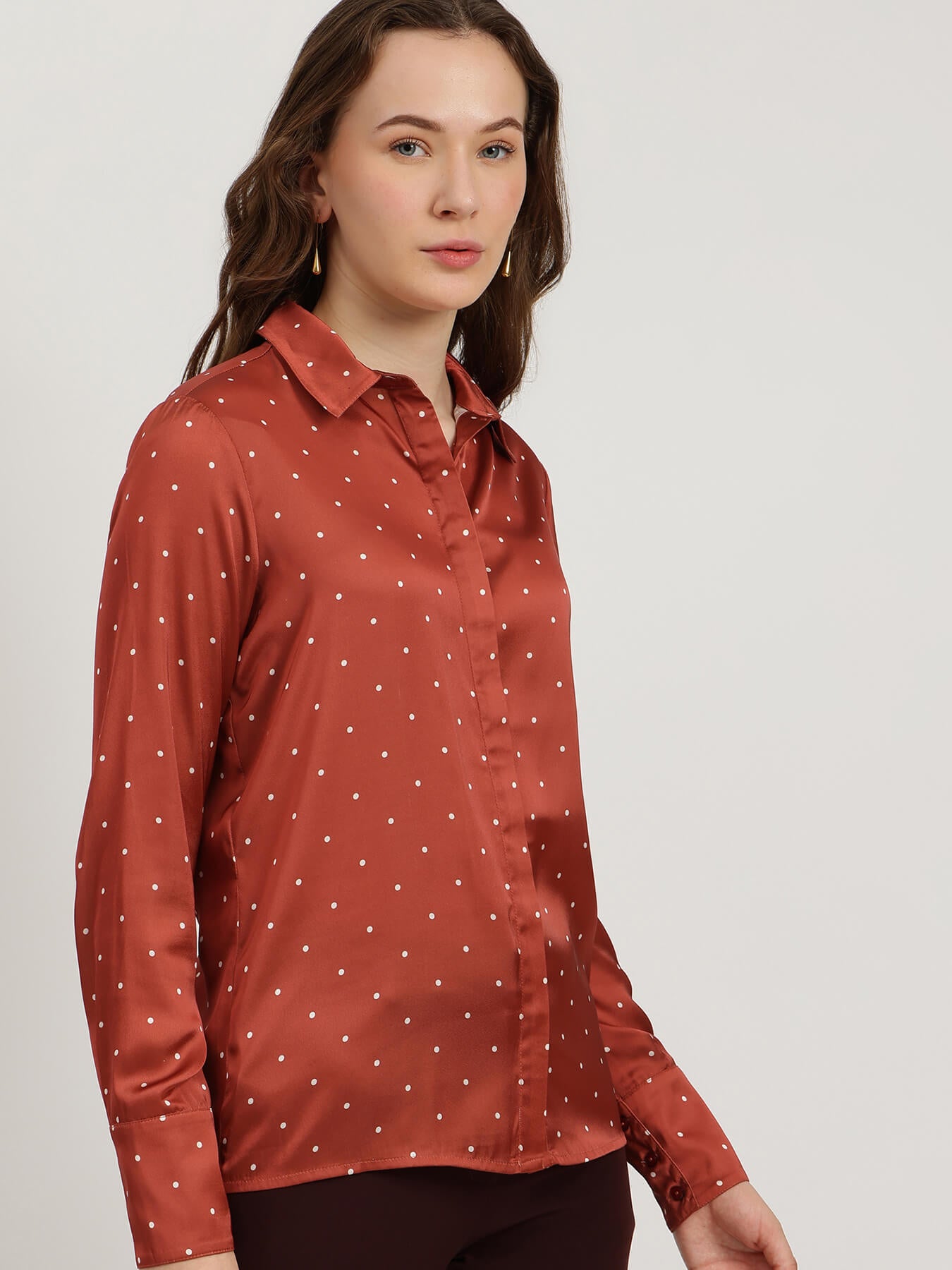 Woman wearing a rust-colored shirt with a subtle pattern on a plain background